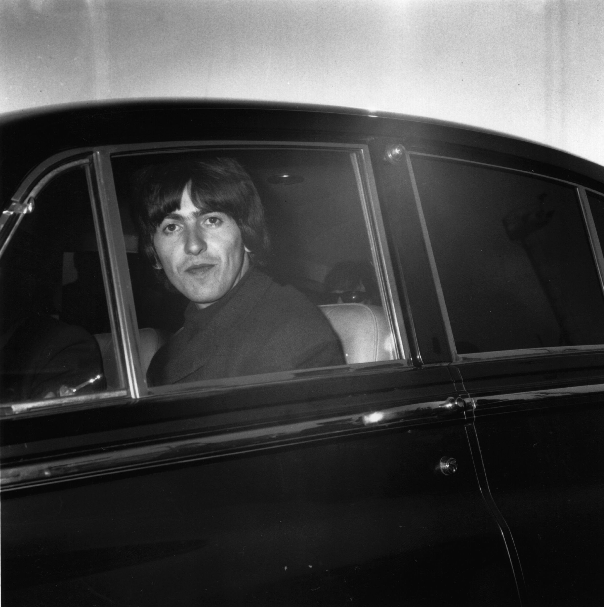 A black and white picture of George Harrison sitting in the back of a car.