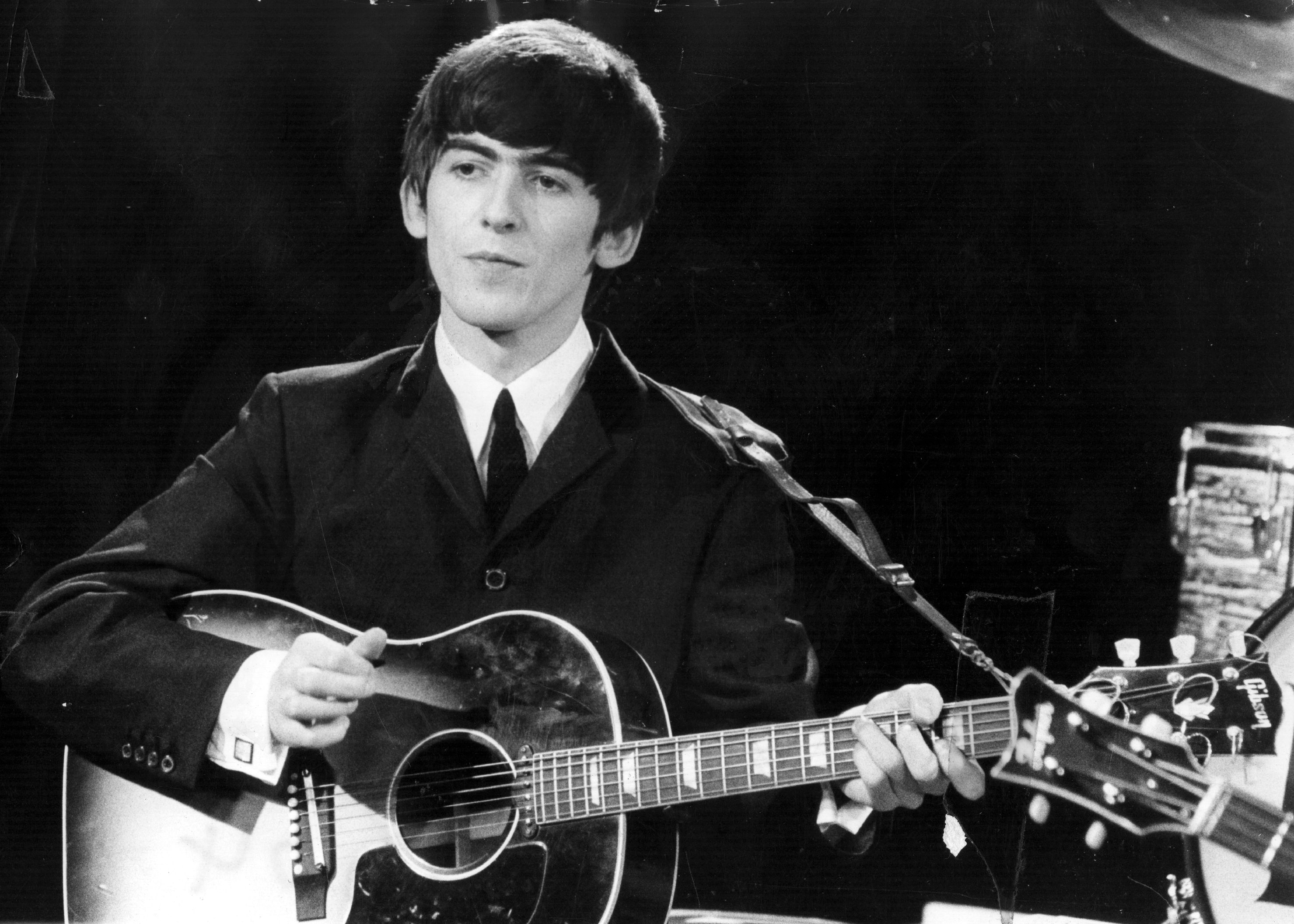 A black and white picture of George Harrison holding a guitar. 