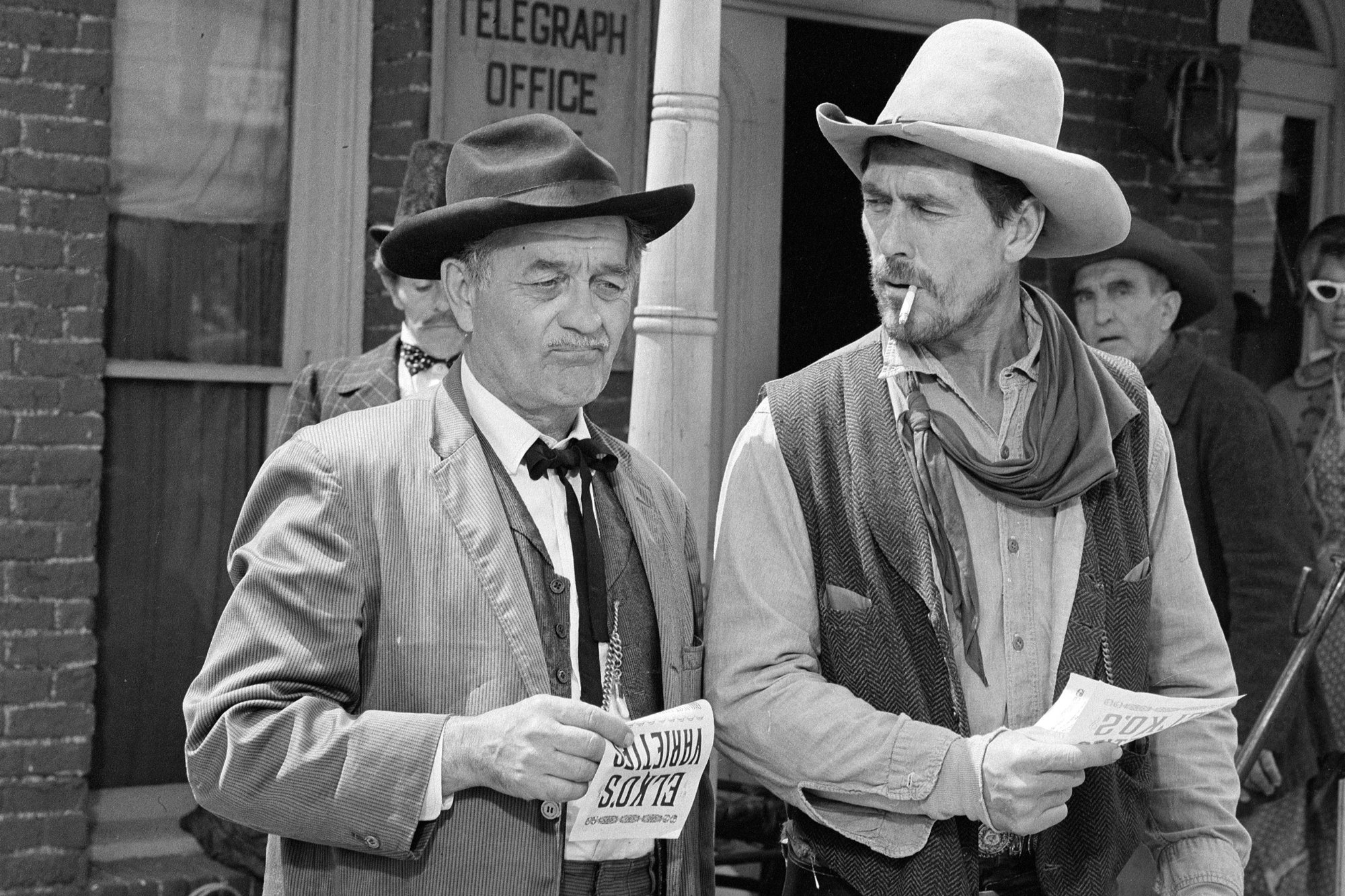 'Gunsmoke' Milburn Stone as Doc Adams and Ken Curtis as Festus Haggen. Curtis look at Stone with a cigarette in his mouth. Both of them are wearing Western costumes.