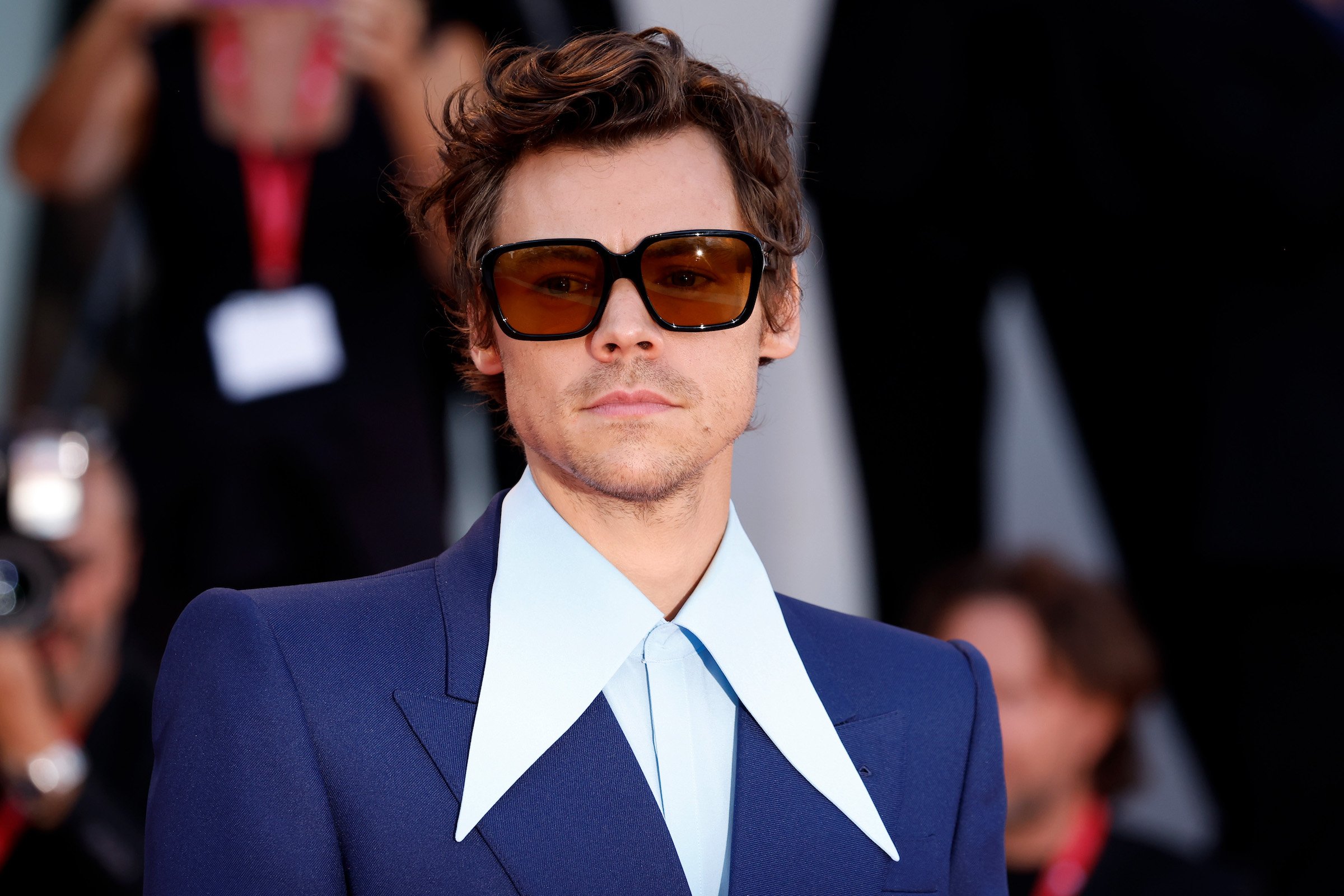 Harry Styles, who is tied with Whitney Houston and Mariah Carey for a Billboard Hot 100 chart record, wearing a blue suit with turquoise collar.