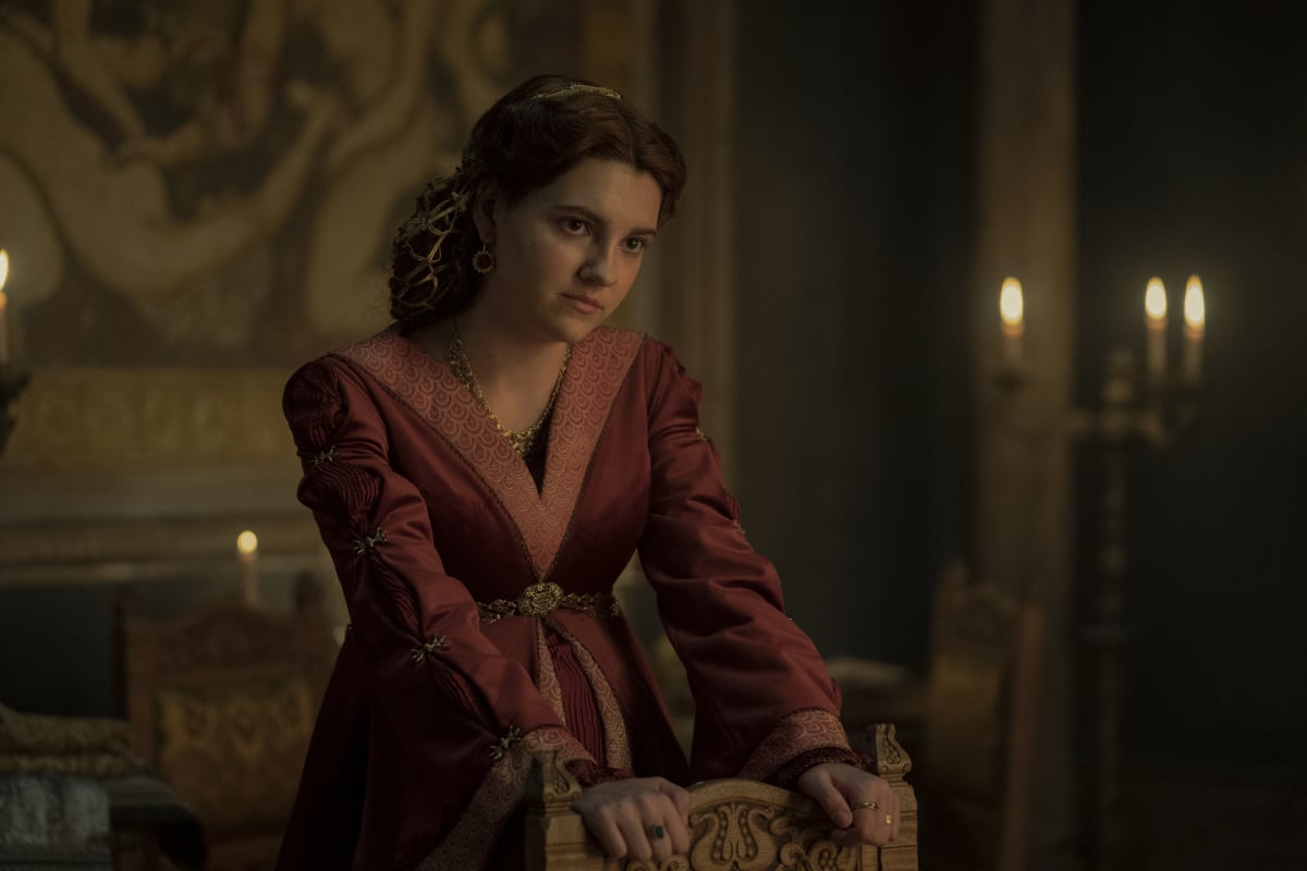 Emily Carey as Alicent Hightower in House of the Dragon. Alicent is pregnant and holds onto the back of a chair, wearing a red dress.
