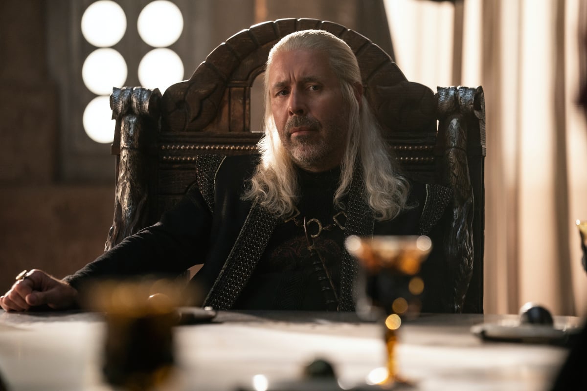 Paddy Considine as King Viserys in House of the Dragon. Viserys sits at a table and looks thoughtful.