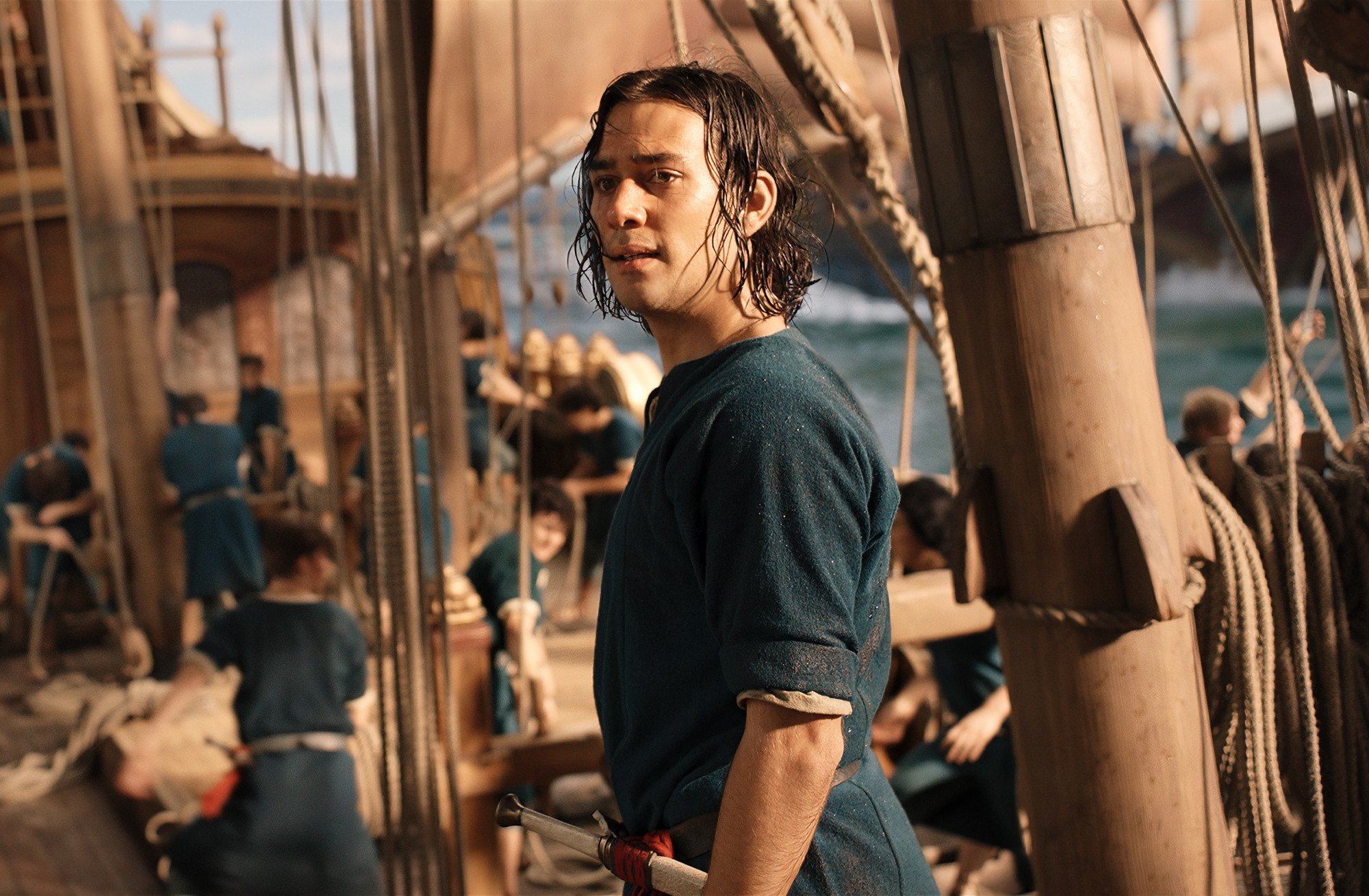 Maxim Baldry as Isildur in 'The Lord of the Rings: The Rings of Power.' He's wearing a blue shirt and standing aboard a ship.
