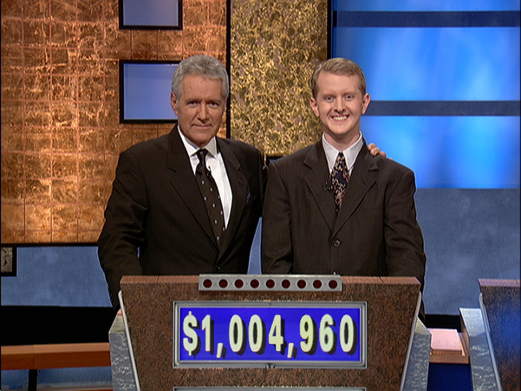 'Jeopardy!' Alex Trebek and casting contestant Ken Jennings. Trebek has his arm around Jennings, who are both wearing suits behind the game podium that reads $1,004,960 on the front.