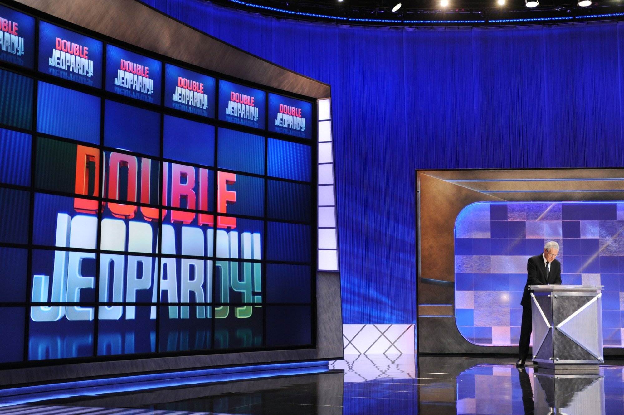 'Jeopardy!' Alex Trebek leading the show before commercial break. He's standing at the podium in a suit with the Double Jeopardy board behind him.