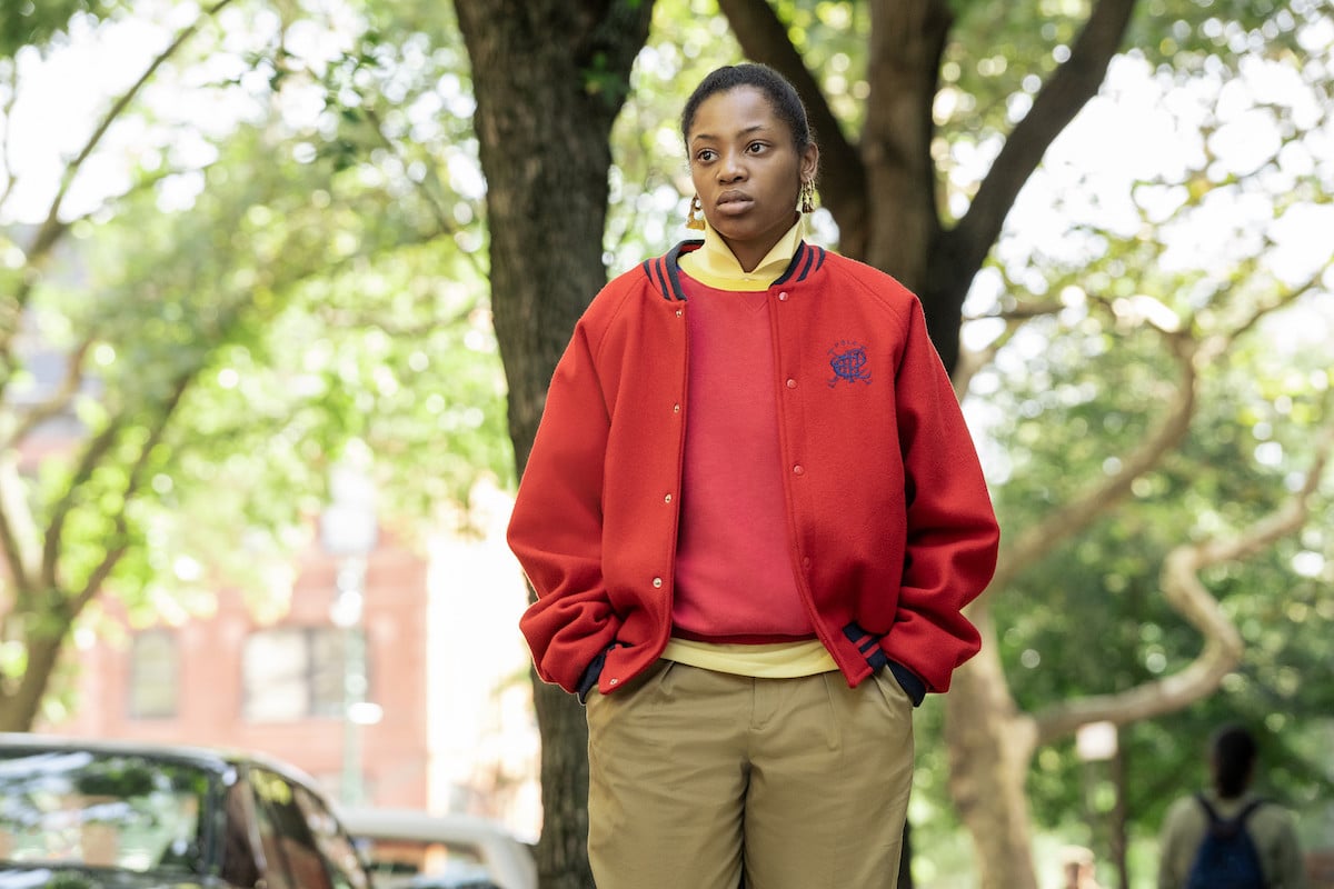 Hailey Kilgore as Jukebox wearing a red jacket and slacks in 'Power Book III: Raising Kanan'