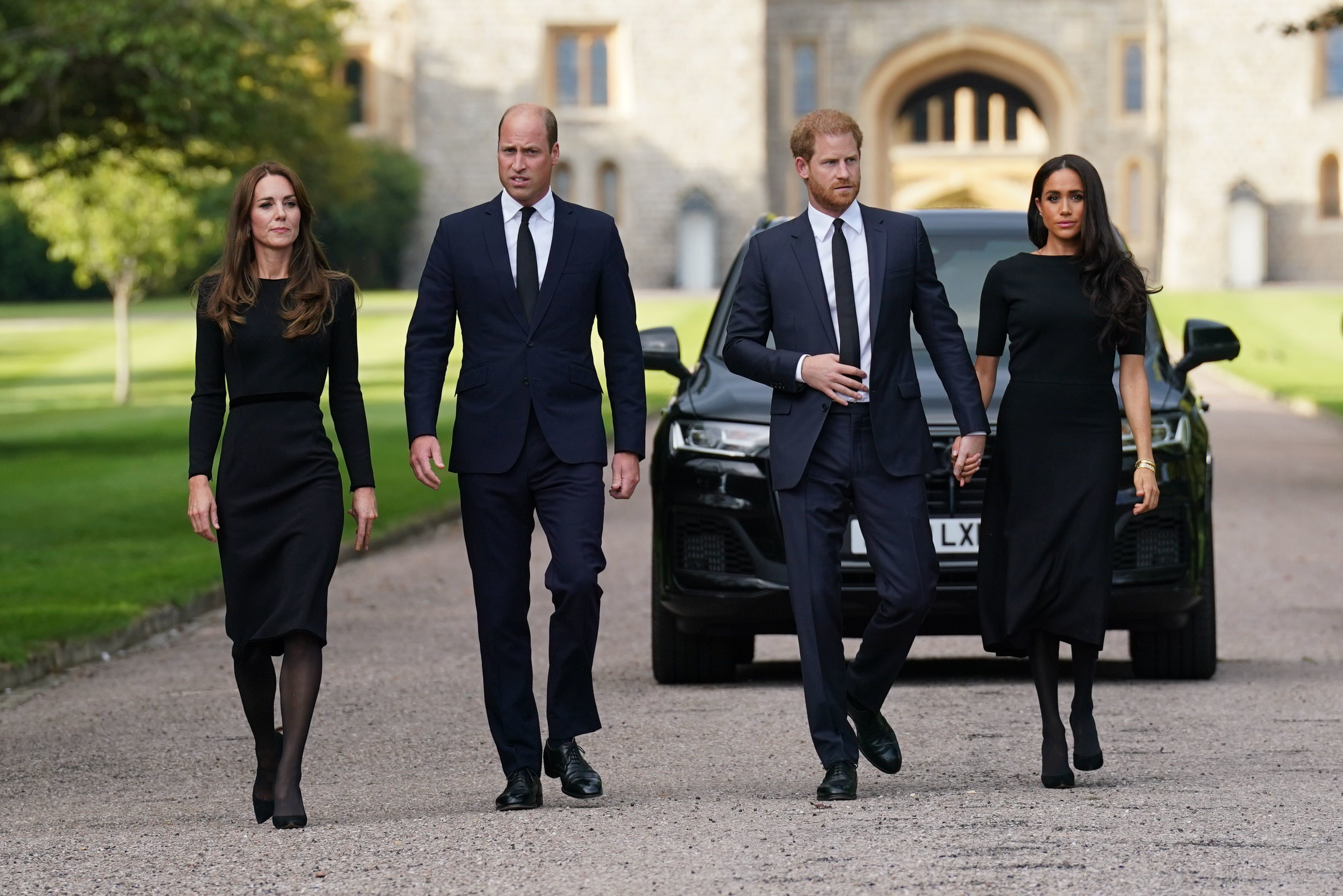 Kate Middleton, Prince William, Prince Harry, and Meghan Markle walk to view tributes left at the gates of Windsor Castle to Queen Elizabeth II
