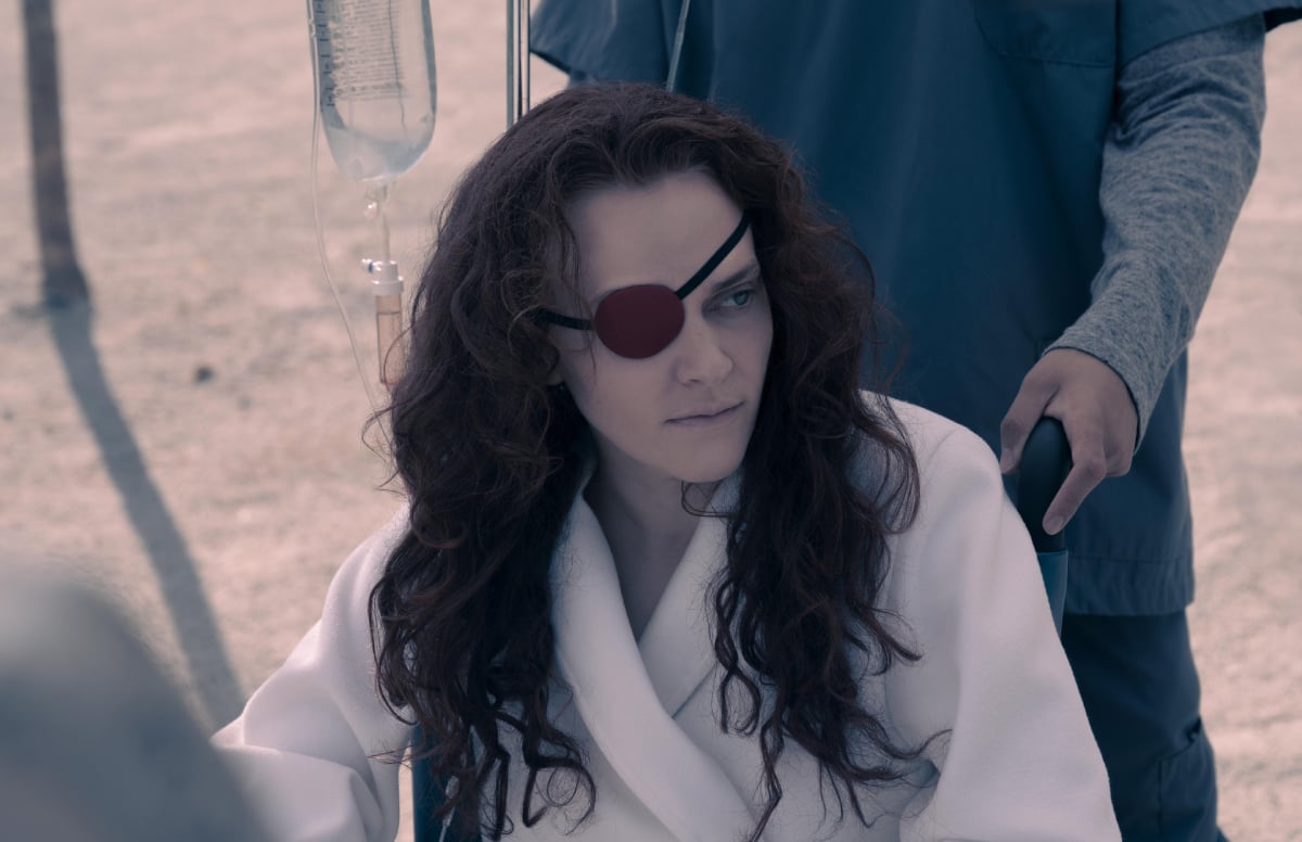 Madeline Brewer as Janine in The Handmaid's Tale Season 5. Janine wears a white robe and eye patch and sits in a wheelchair.