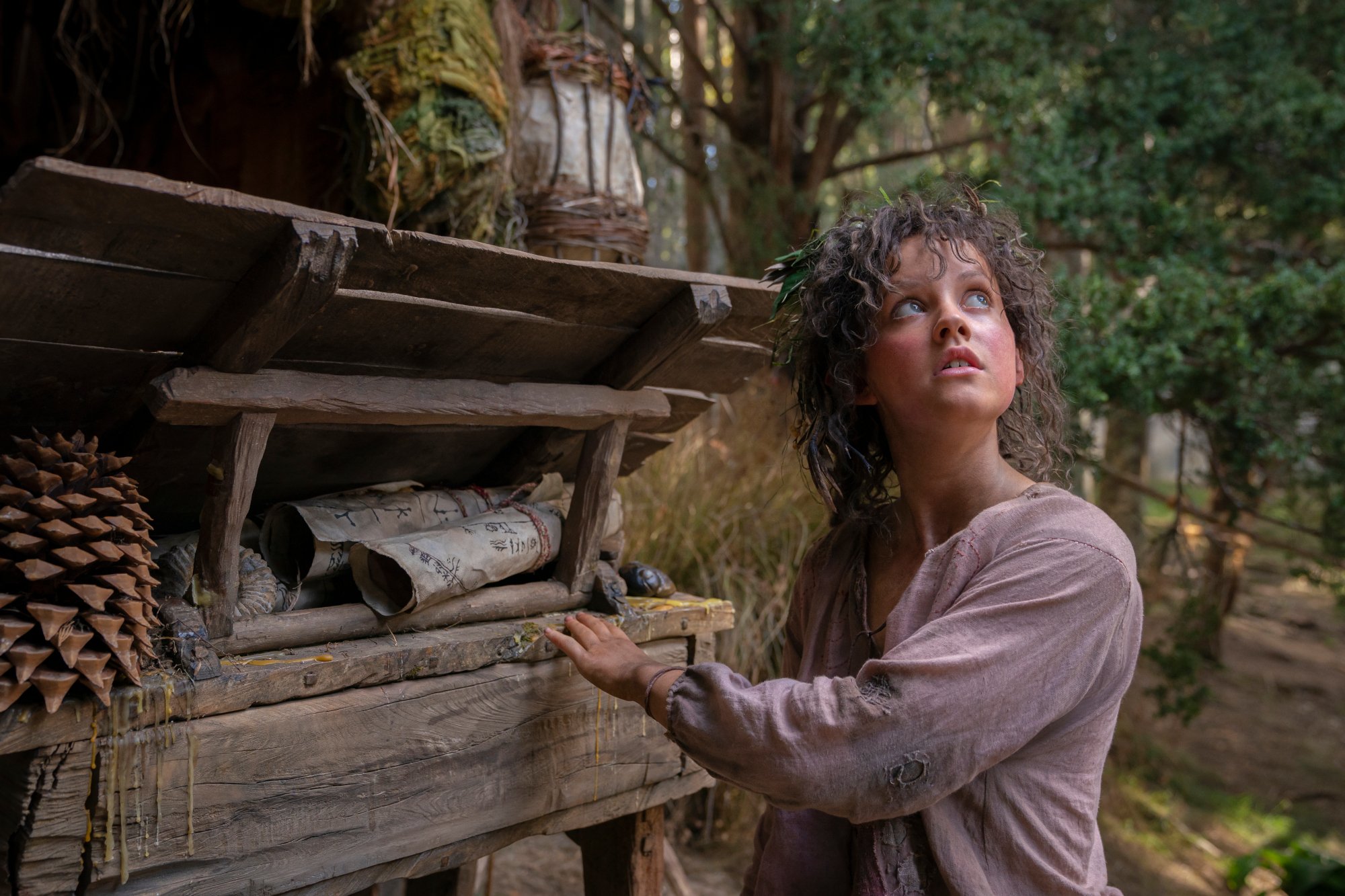 Markella Kavenagh as Nori Brandyfoot in 'The Lord of the Rings: The Rings of Power.' She's holding onto something made of wood and looking upwards