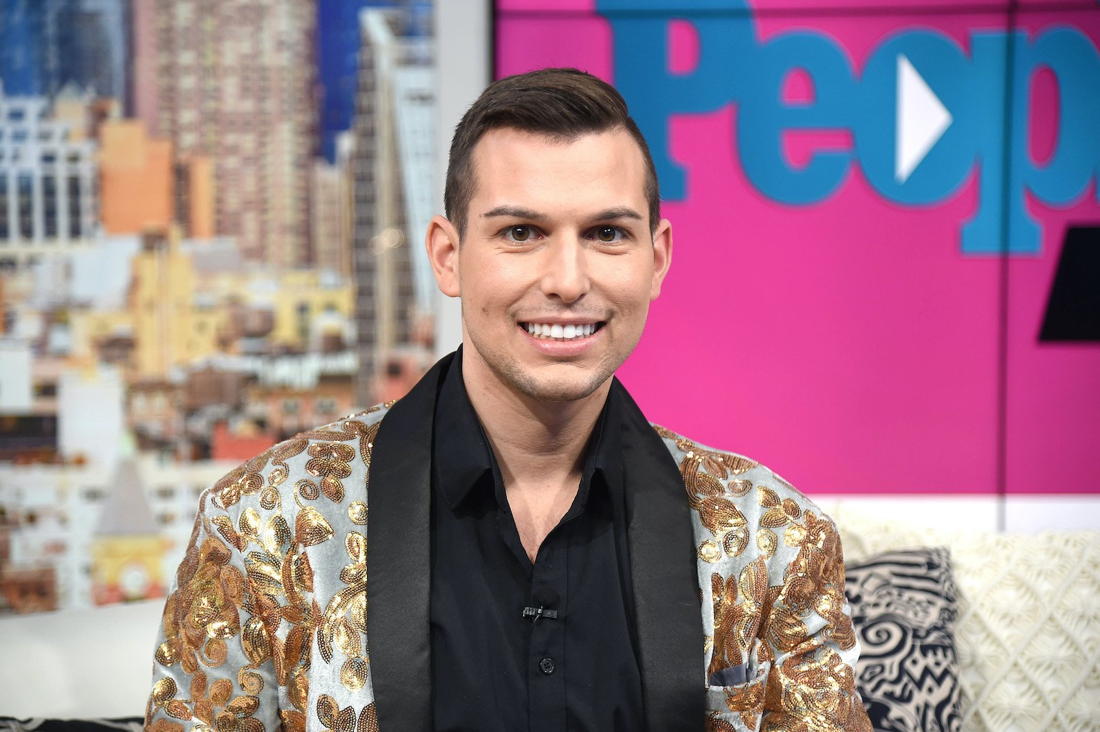 Reality TV star and psychic medium Matt Fraser smiles for the camera wearing a gold and white jacket. 