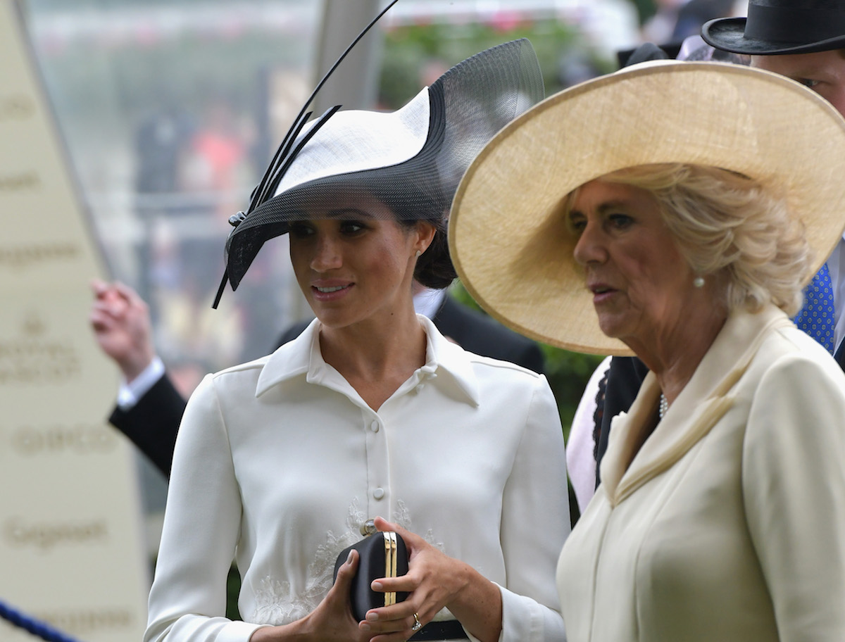Meghan Markle, not noticing Camilla Parker Bowles serving up recipes from Together: Our Community Cookbook during a lunch, stood next to Camilla Parker Bowles