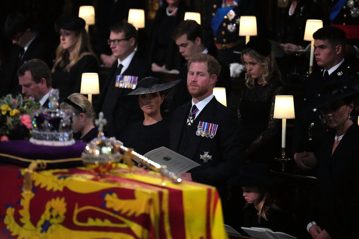 Prince Harry and Meghan Markle, who sat in the second row at Queen Elizabeth's funeral reportedly due to age order seating arrangements, stand in the front row as As Queen Elizabeth's coffin passes them at St. George's Chapel