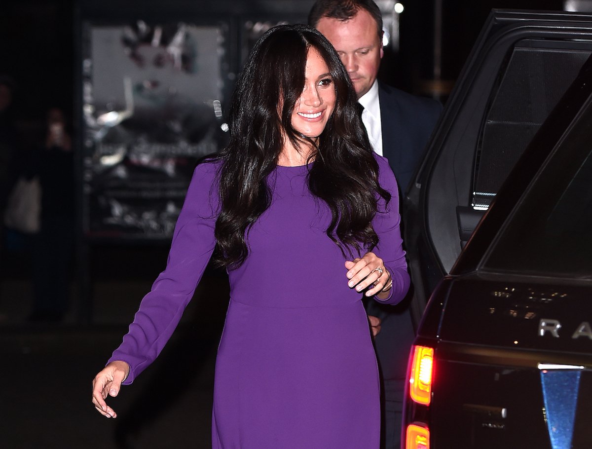 Meghan Markle, who a body language expert says exhibited signs of wanting to 'cut off' people at the 2019 One Young World opening ceremony, smiles wearing a purple dress