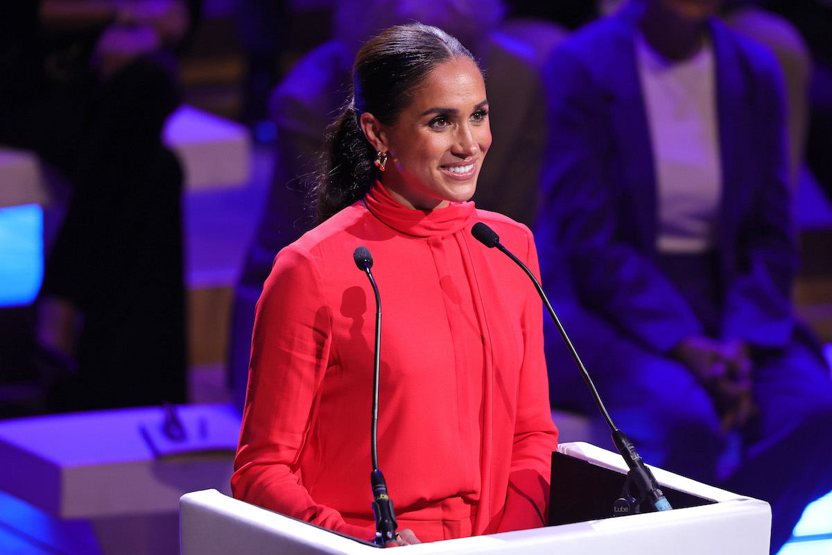 Meghan Markle, who a royal commentator says 'made no sense' to young audience members at the 2022 One Young World Summit opening ceremony during speech, smiles wearing red while standing at a microphone