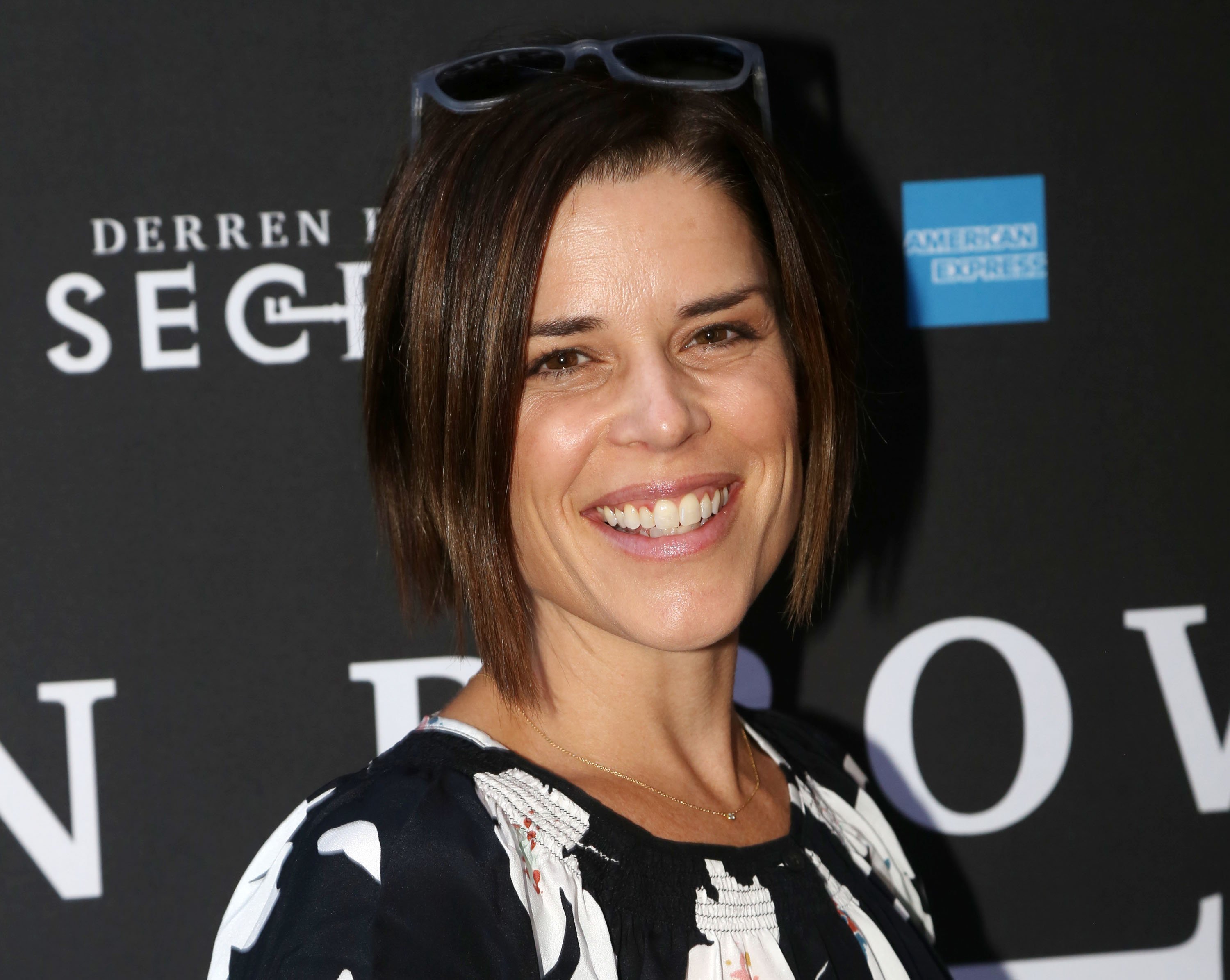 smiling Neve Campbell with sunglasses on her head