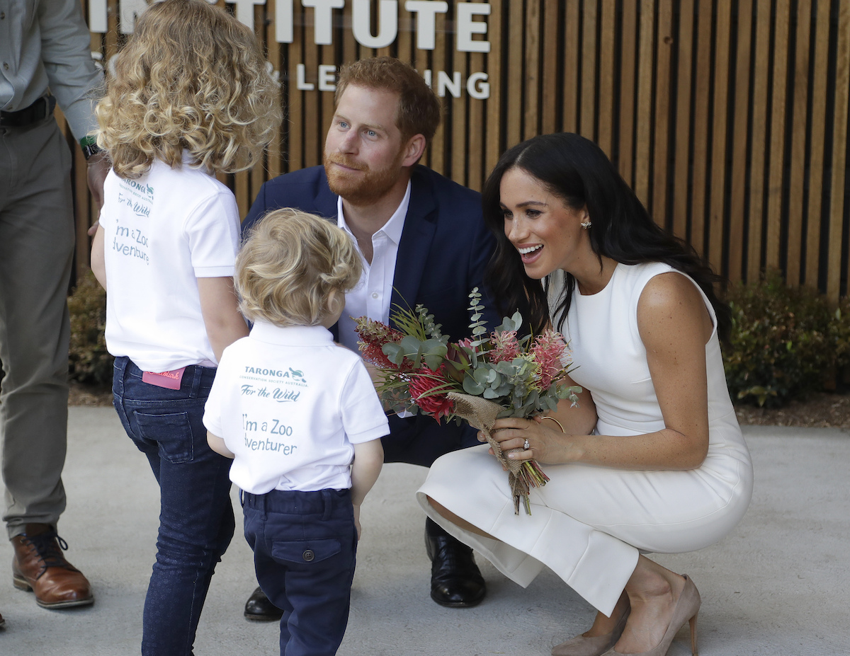 Prince Harry and Meghan Markle, who a commentator said people are 'annoyed' by because she challenges their idea of what it means to be a princess, crouch down to greet children