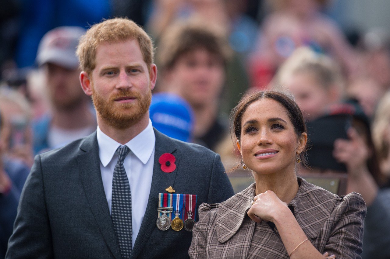 Prince Harry and Meghan Markle stand next to each other and smile.