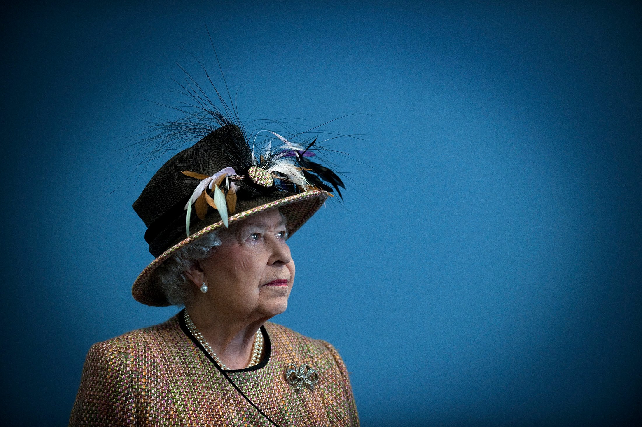 Queen Elizabeth II looks up in front of a blue background. 