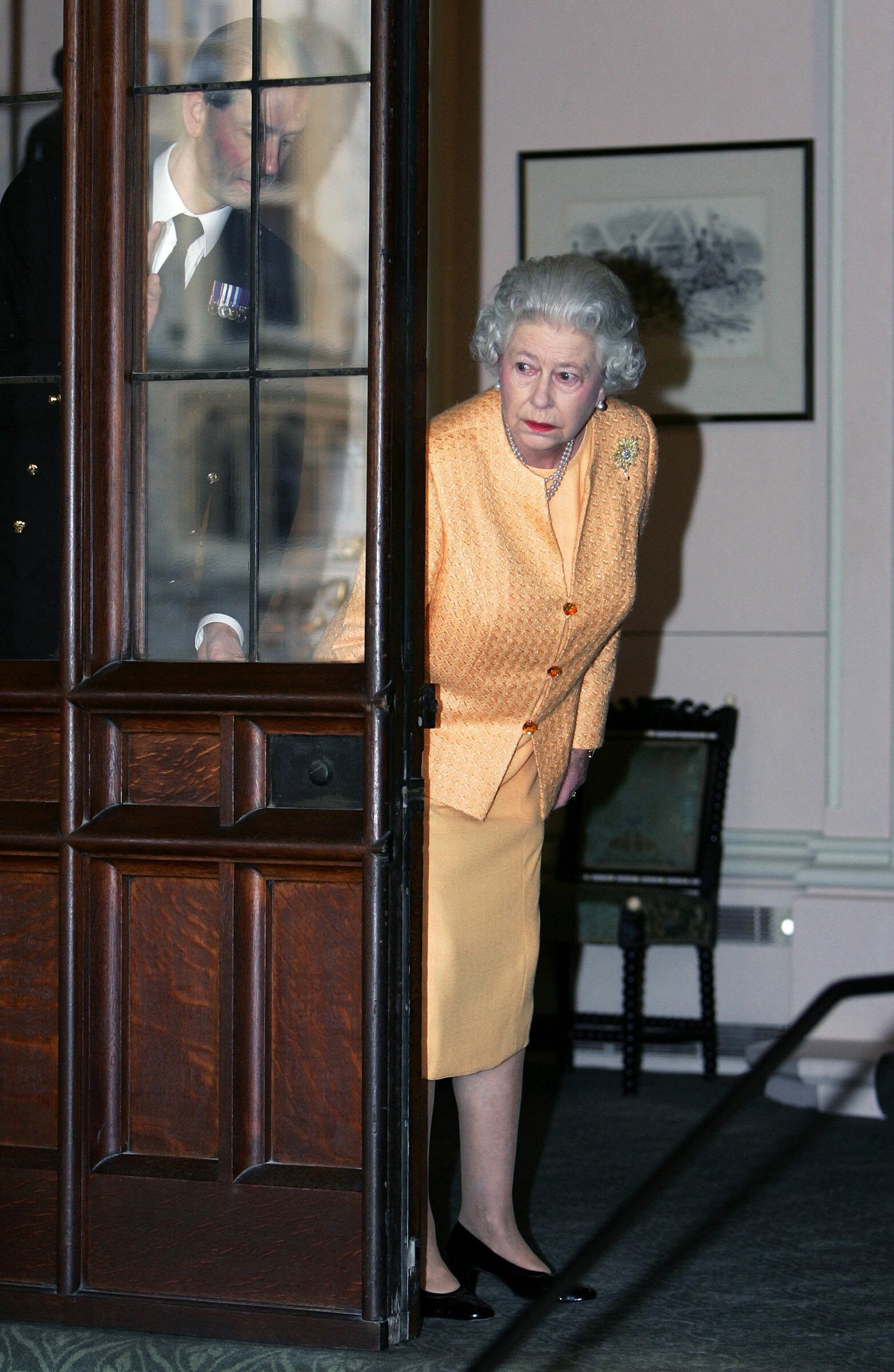 Królowa Elżbieta II i jej adiutant Paul Whybrew zaglądają przez drzwi, aby zobaczyć, czy podjechał samochód
