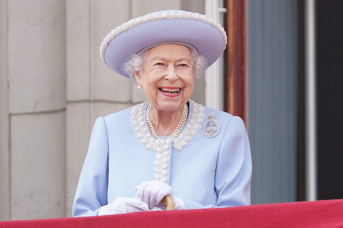 Queen Elizabeth smiles in a photo from her reign wearing a purple outfit