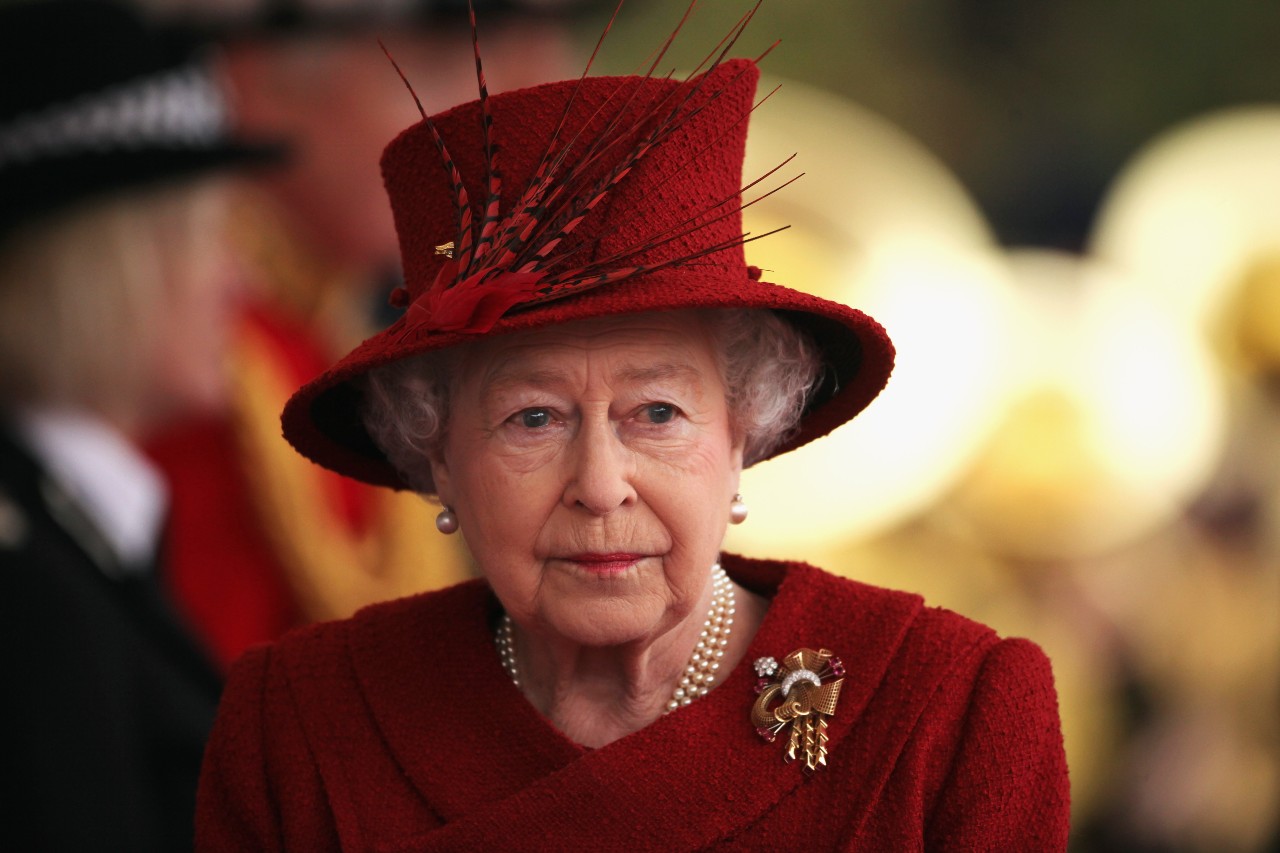 Queen Elizabeth II wears a red outfit and hat.