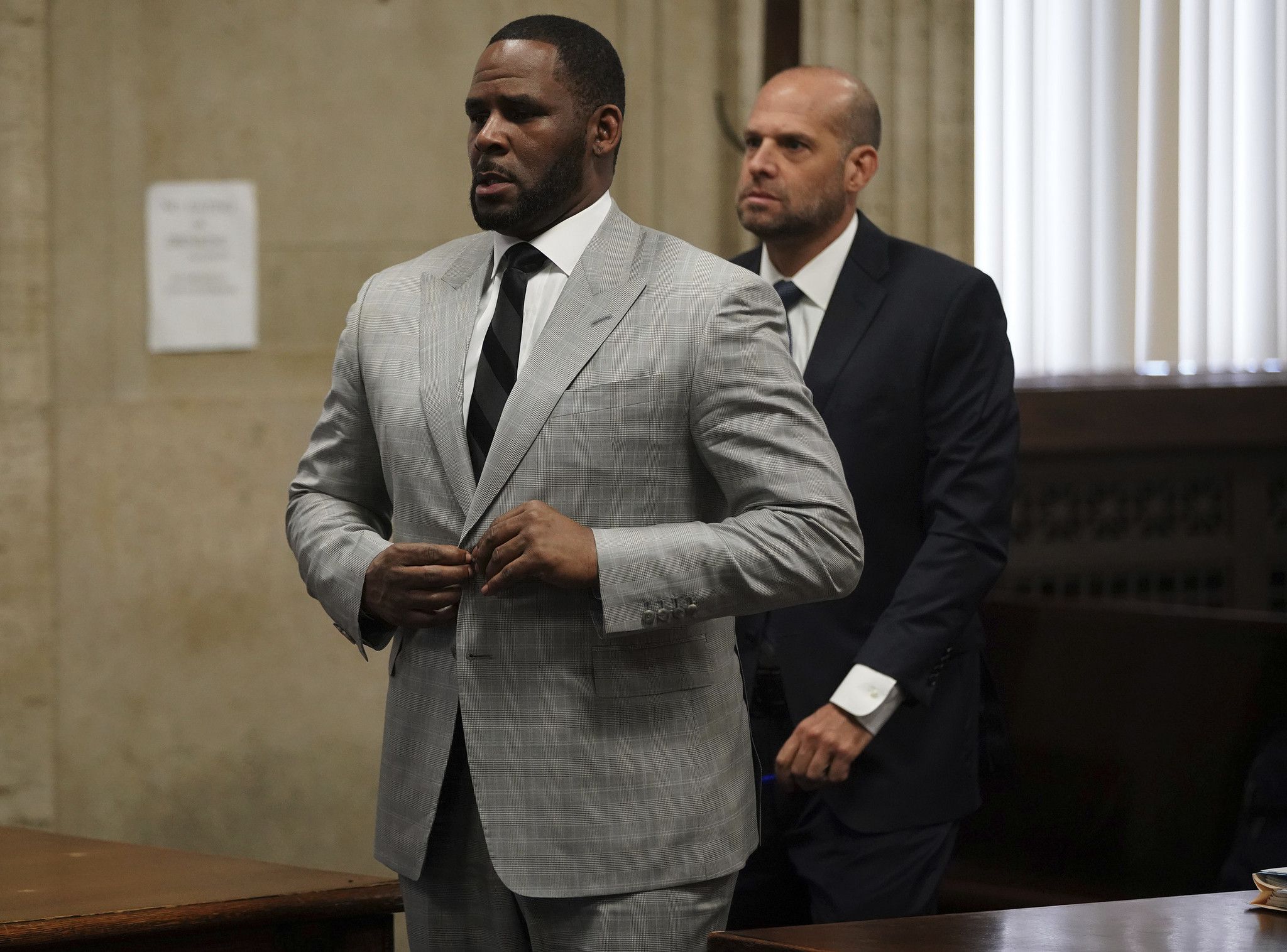 R. Kelly buttons up his suit jacket in court; Kelly is ordered to pay restitution to his victims