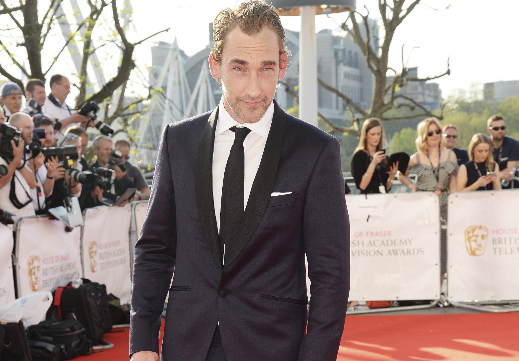 Actor Joseph Mawle, who plays Adar in 'The Lord of the Rings: The Rings of Power.' He's wearing a black suit, white shirt, and black tie and smiling.