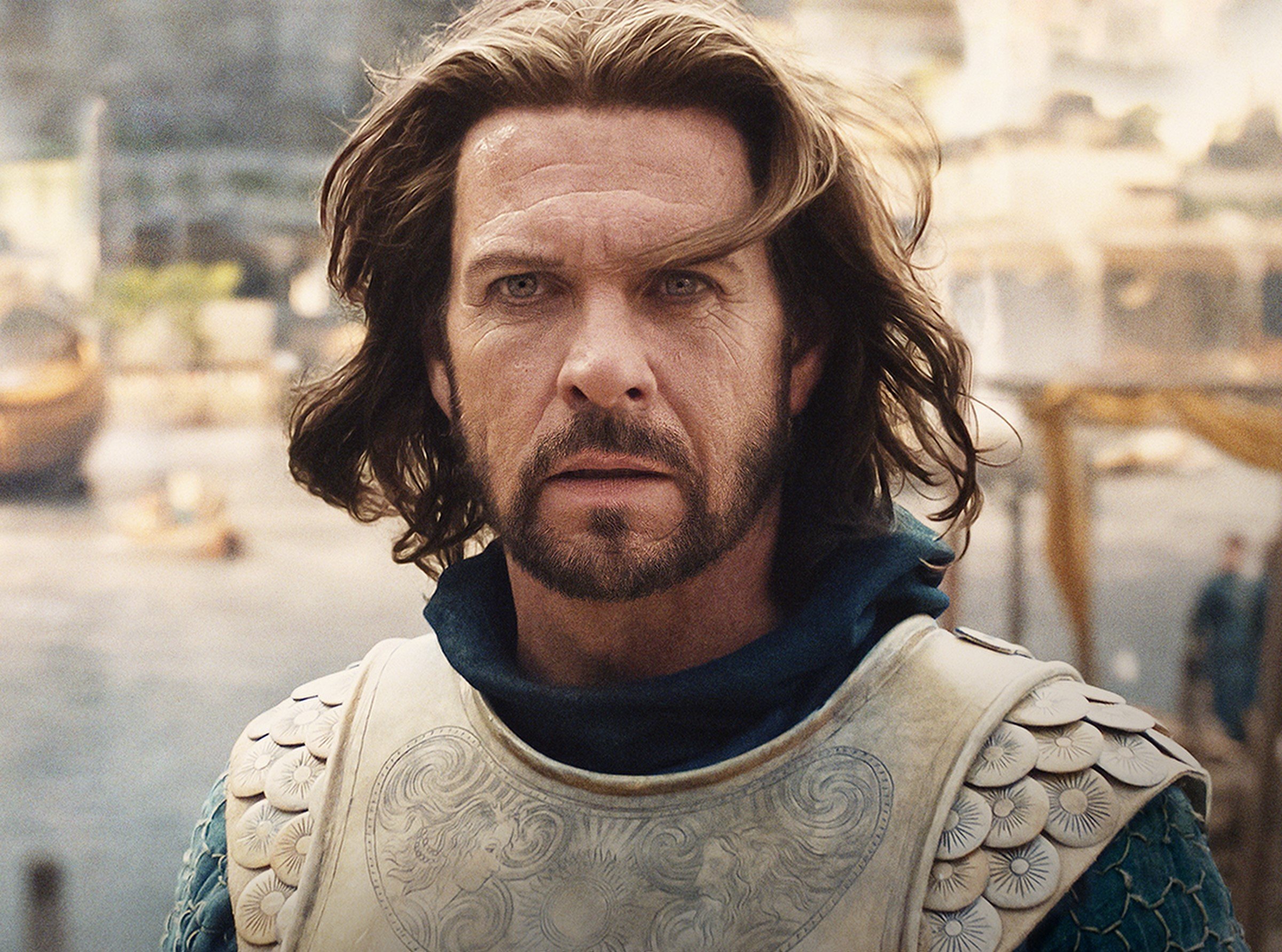 Lloyd Owen as Elendil in 'The Lord of the Rings: The Rings of Power.' His hair is blowing in the wind, and he's wearing golden armor.