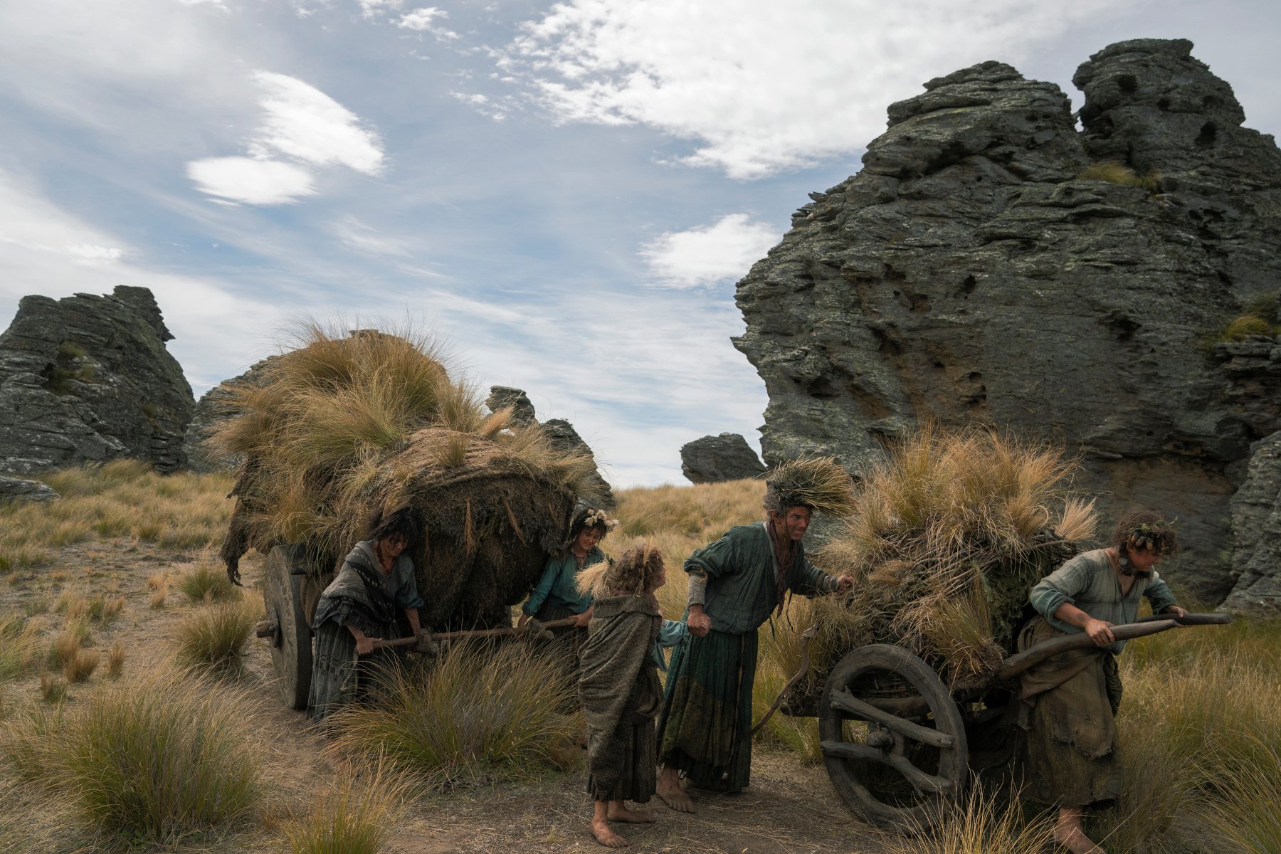 The Harfoots in 'The Rings of Power' Episode 5 for our article about its Easter Eggs. They're walking on grass and pulling carts behind them.