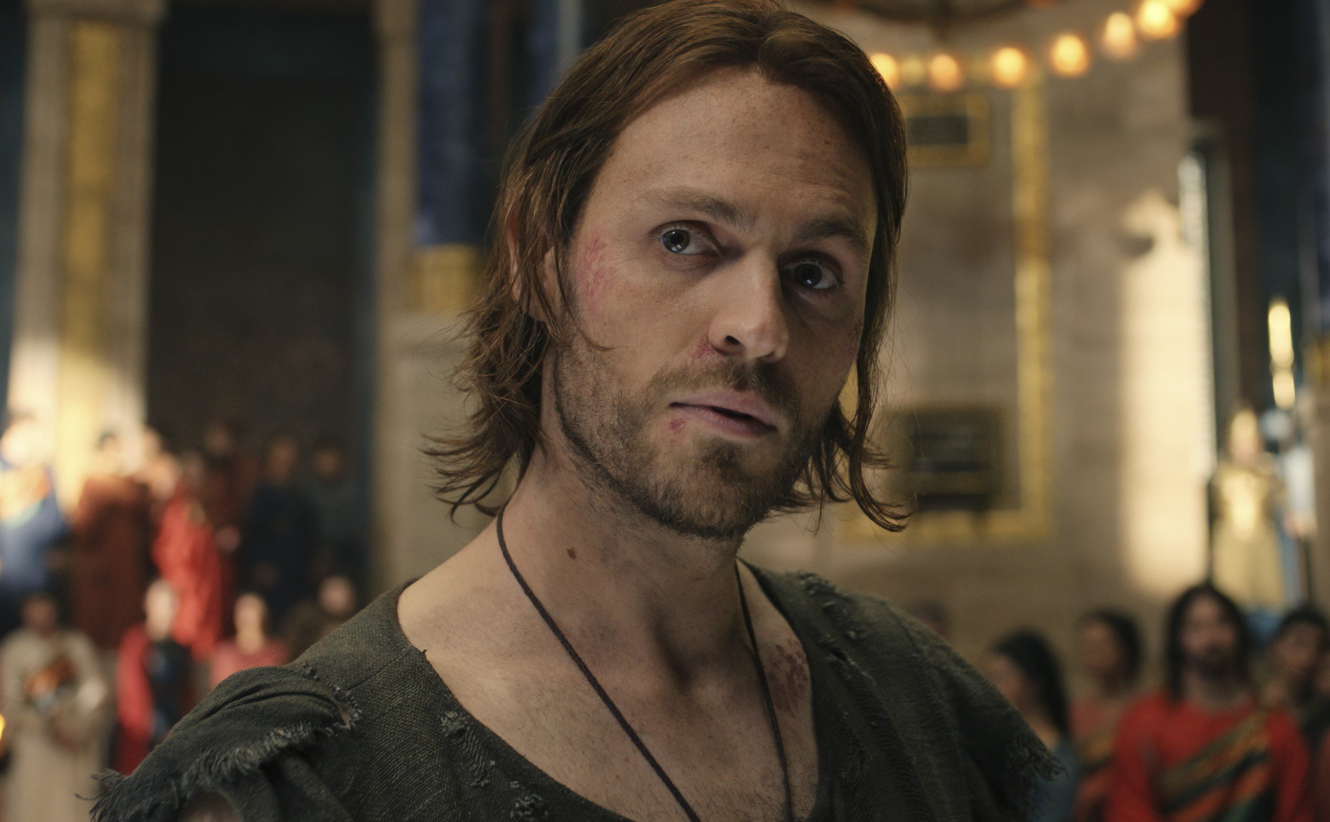 Charlie Vickers as Halbrand in 'The Lord of the Rings: The Rings of Power' Episode 3. He's wearing something around his neck, his hair looks wet, and he's staring at someone off-screen.