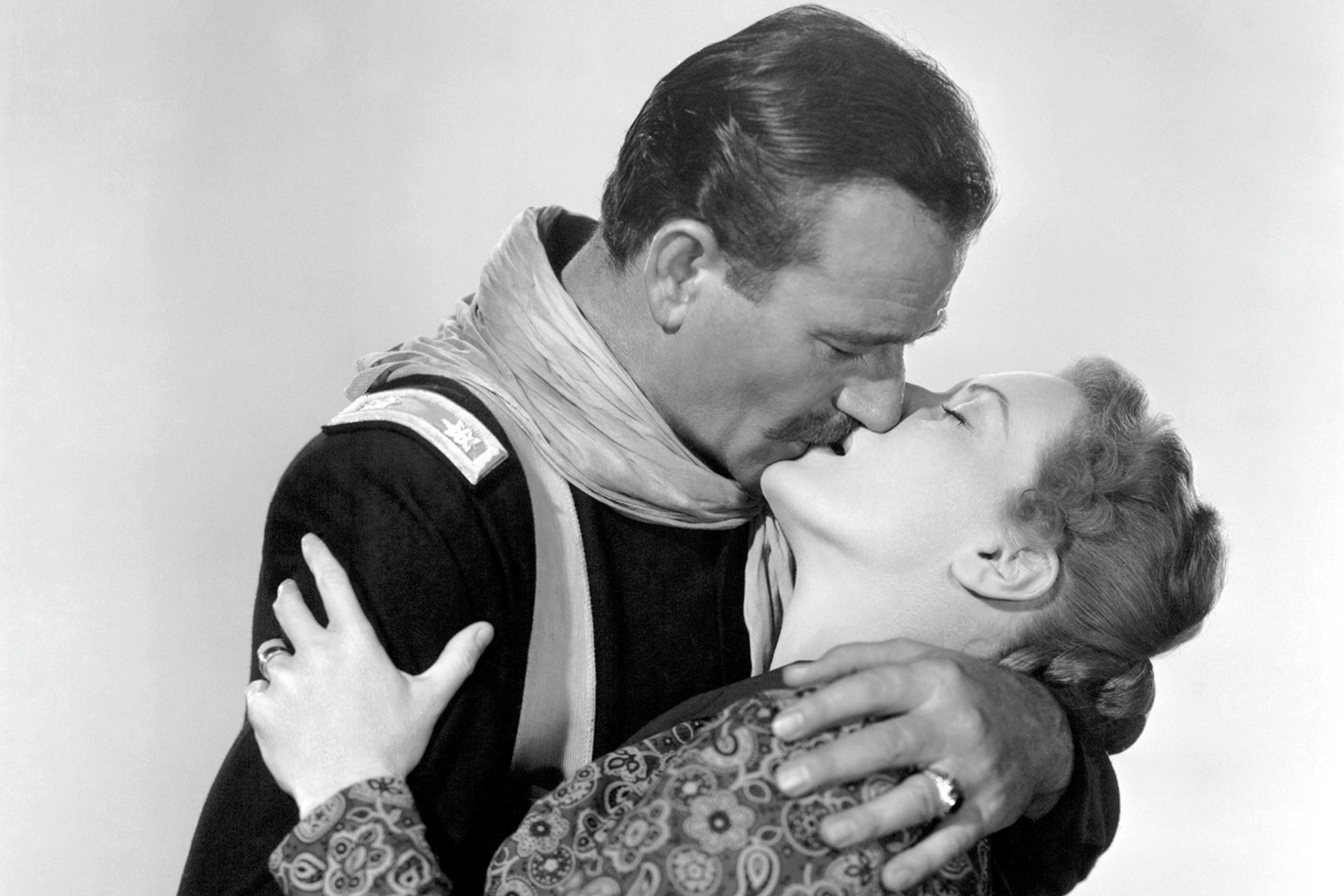 John Wayne and Maureen O'Hara embracing one another while kissing.