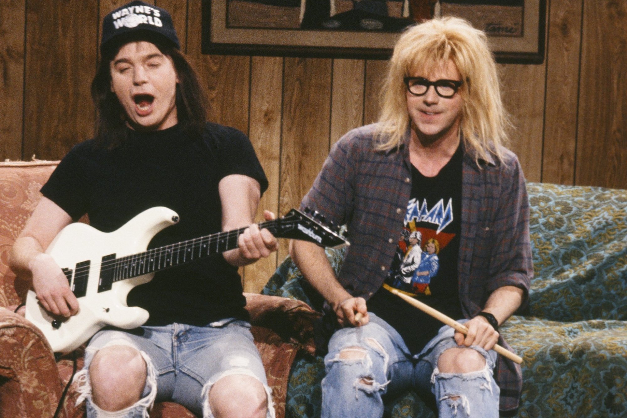'Saturday Night Live' 'Wayne's World' Mike Myers as Wayne Campbell and Dana Carvey as Garth Algar. They're sitting on the couch with Myers holding a guitar and Carvey holding drumsticks.