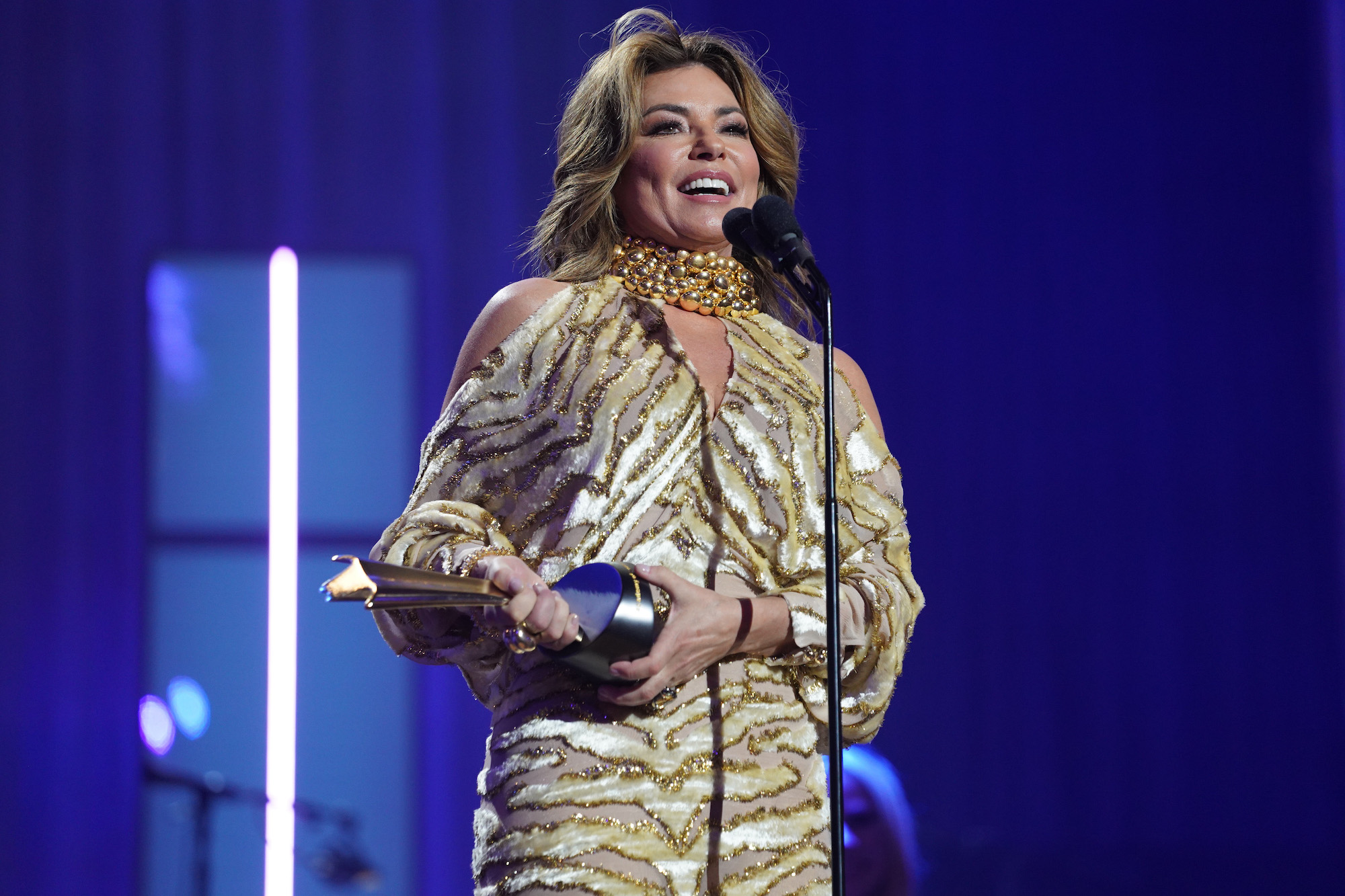 Shania Twain, who sang as a hotel singer before becoming a global superstar, wearing gold and accepting an award.