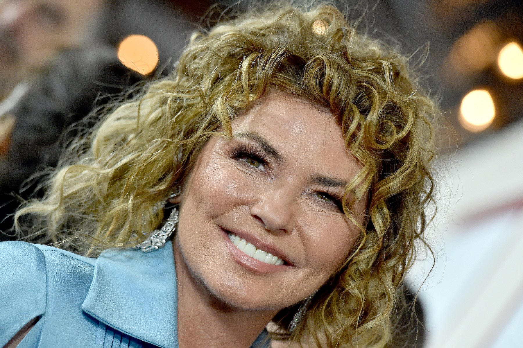 Shania Twain, who has peed on stage multiple times, wearing turqoise and smiling for a photo