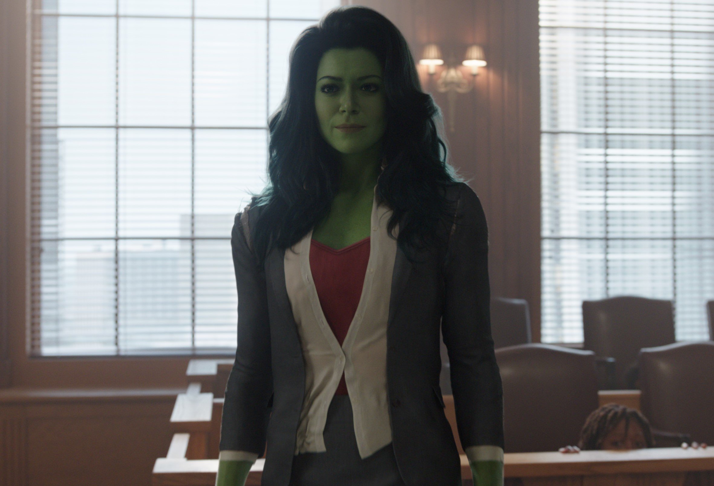 Tatiana Maslany in Marvel's 'She-Hulk,' which may have introduced The Wrecking Crew in episode 3. In the photo, she's standing in a courtroom, is tall and green, and is wearing a white blouse and gray blazer.