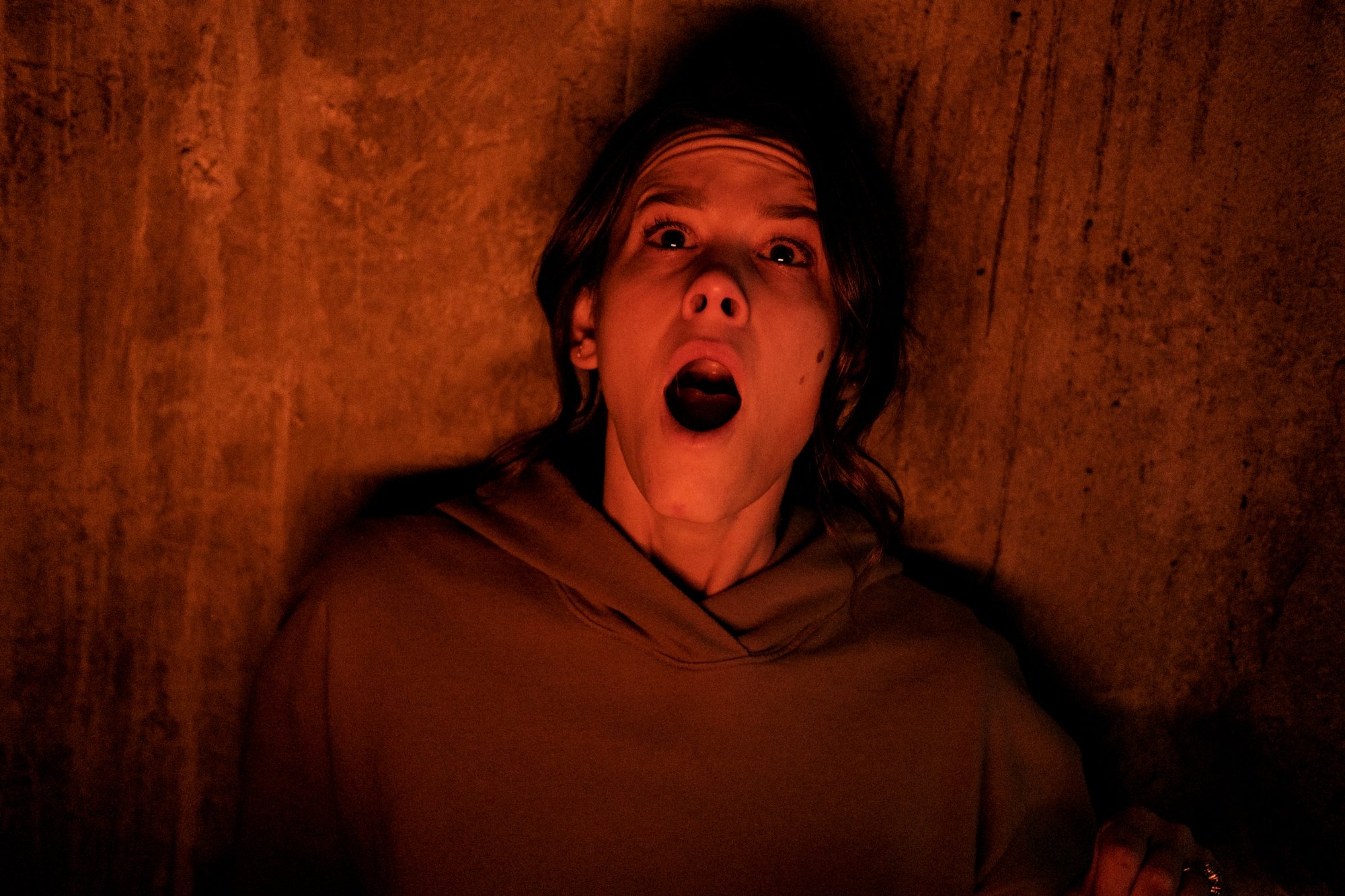 'Smile' Sosie Bacon as Dr. Rose Cotter. She's laying on a wooden floor wearing a hoodie with her jaw dropped in shock.