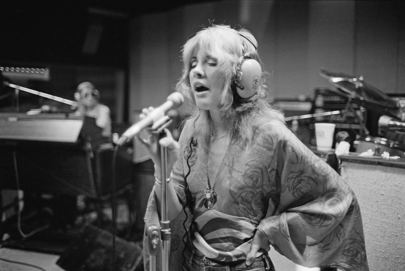 A black and white picture of Stevie Nicks wearing headphones and standing in front of a microphone. 