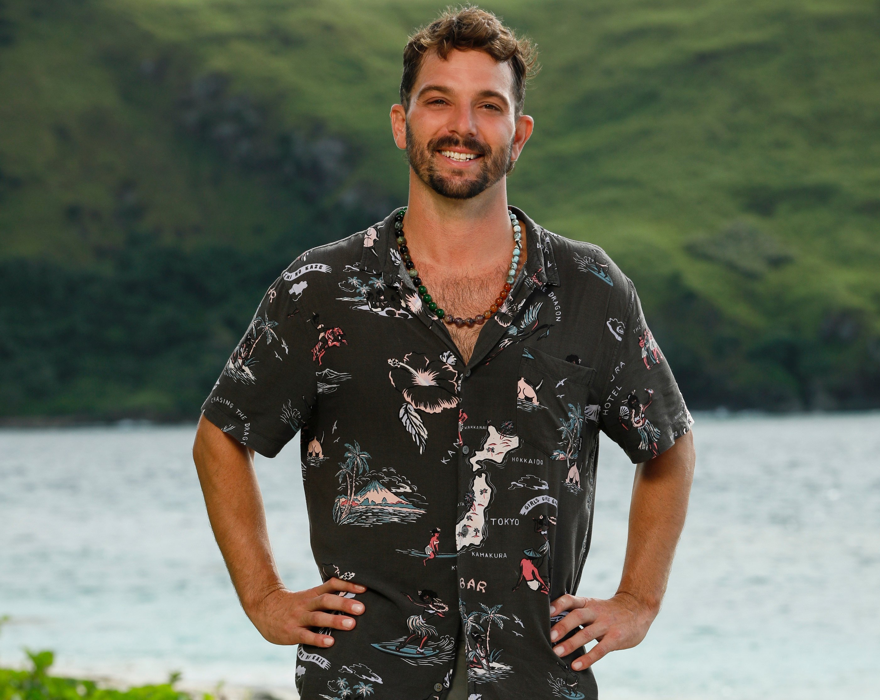 Cody Assenmacher from 'Survivor Season 43' stands in a t-shirt on the beach.