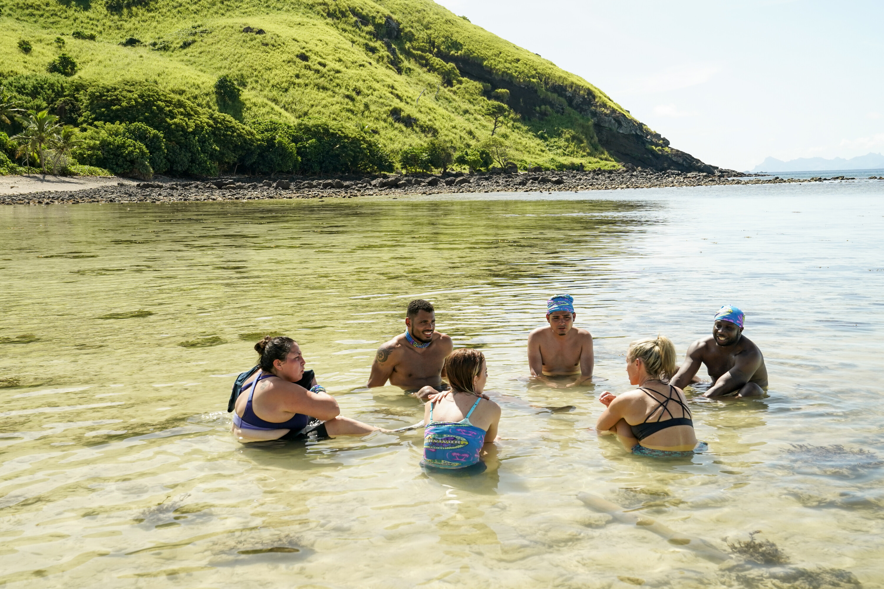 The Coco tribe — Karla Cruz Godoy, Ryan Medrano, Geo Bustamante, Cassidy Clark, Lindsay Carmine, and James Jones — sit in a circle in shallow waters in 'Survivor' Season 43, which premieres tonight, Sept. 21, on CBS.
