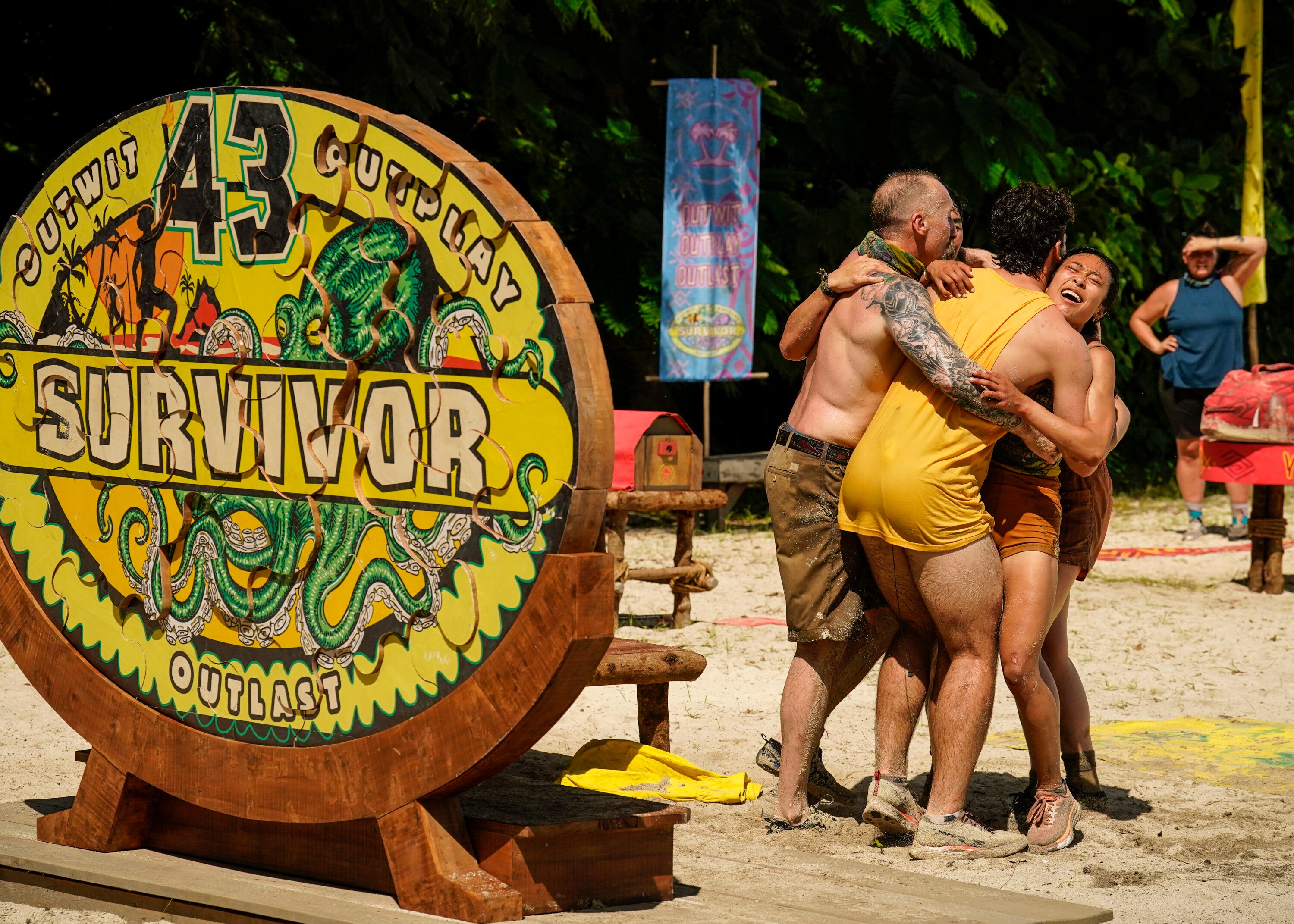 Mike Gabler, Sami Layadi, and Jeanine Zheng, who are a part of the Baka tribe, celebrate with their fellow tribemates following a 'Survivor' Season 43 challenge. The group is hugging.