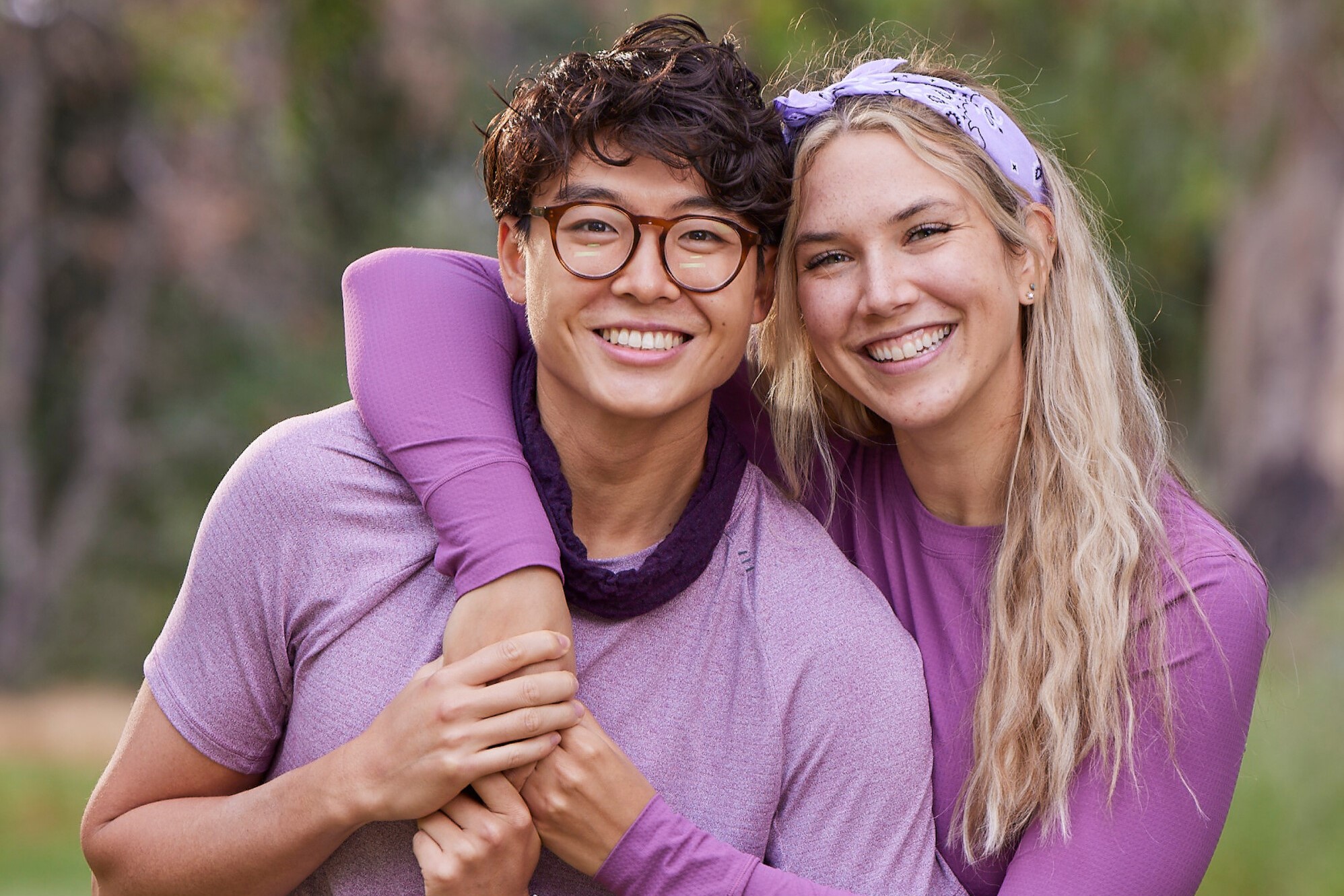 Derek Xiao and Claire Rehfuss, who star in 'The Amazing Race' Season 34 on CBS, pose for promotional pictures. Derek wears a light purple shirt. Claire wears a purple long-sleeved shirt.