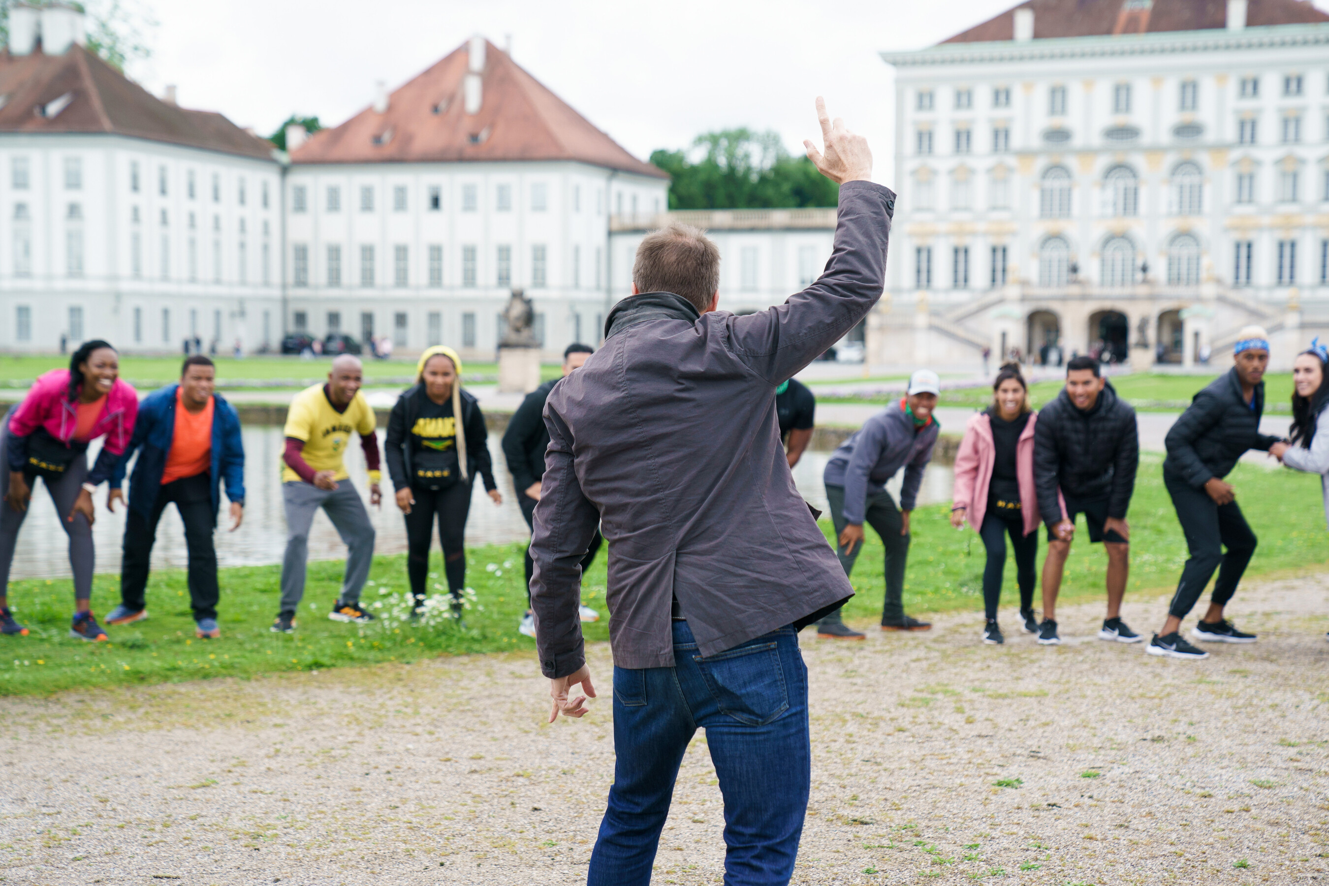'The Amazing Race' Season 34 cast and host Phil Keoghan gather before beginning the first leg. The racers are crouched, ready to run, while Phil, who wears a dark gray jacket and jeans, holds up his arm to signal when they can start.