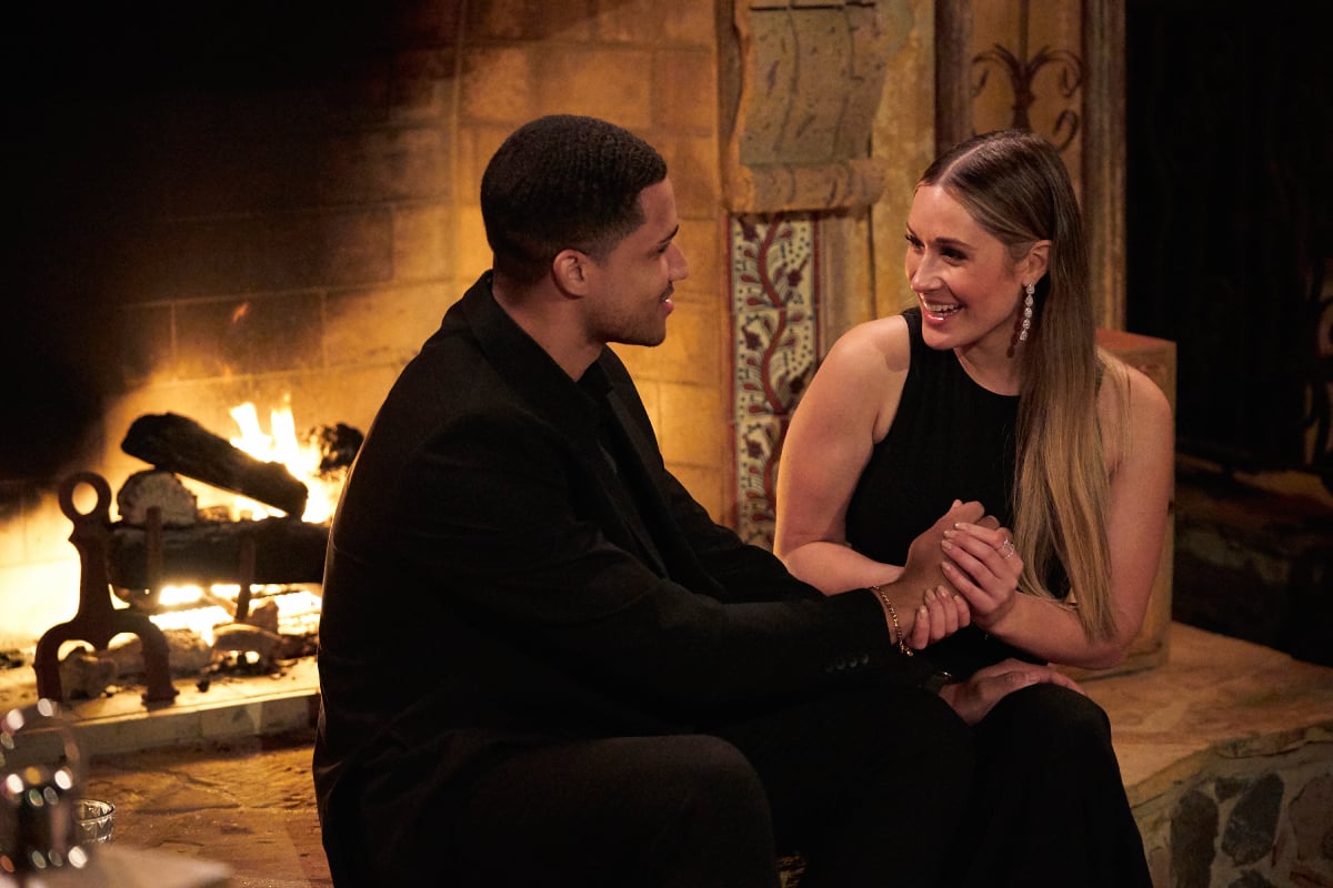 Aven Jones and Rachel Recchia on The Bachelorette. Aven and Rachel talk by the fireplace. They are both wearing all-black outfits. 