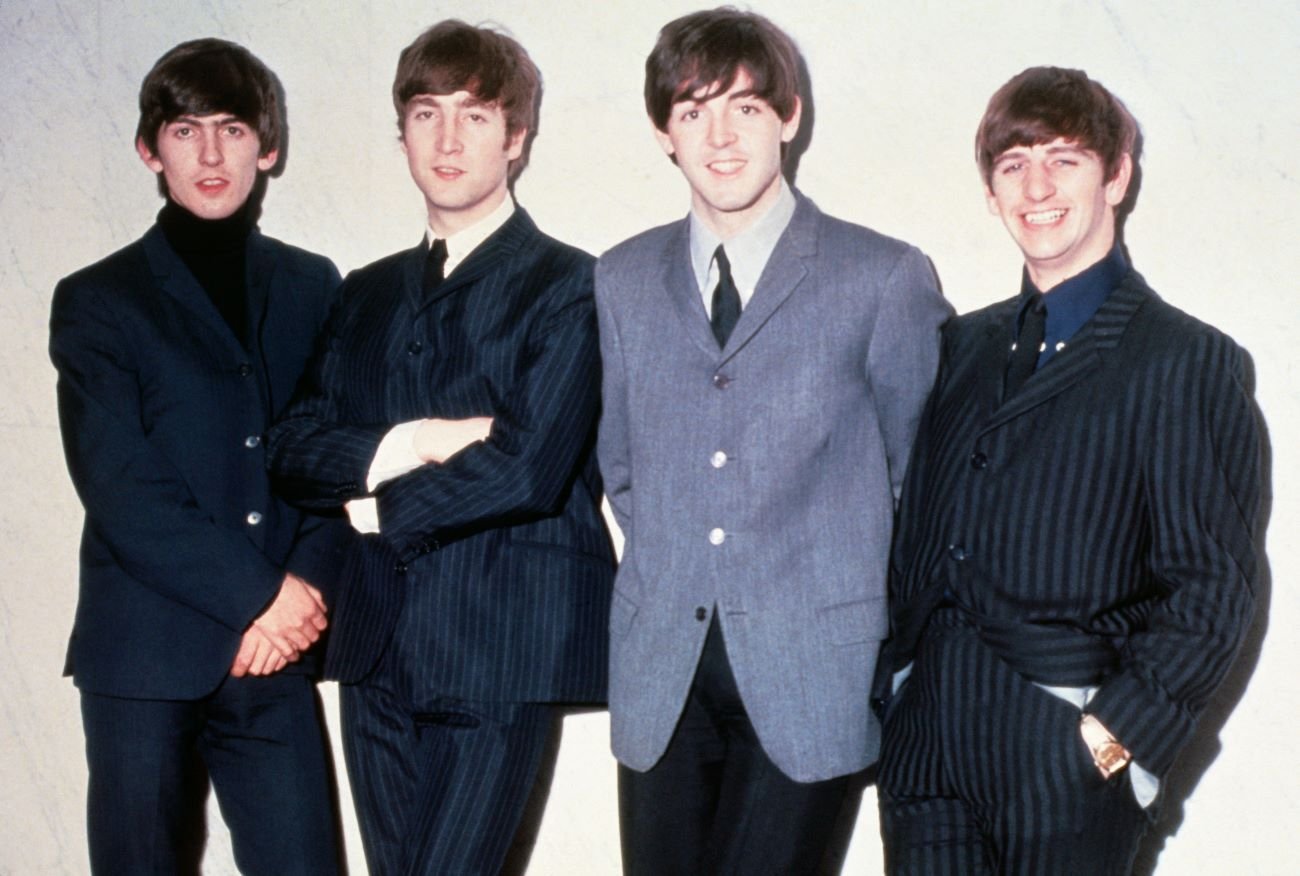 The Beatles pose together while standing against a wall.