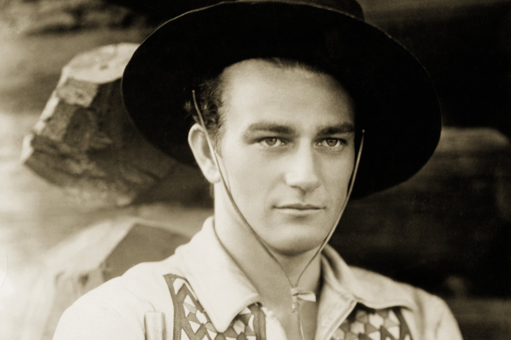 'The Big Trail' actor John Wayne wearing a cowboy hat and Western costume. The photo is in sepia tone.