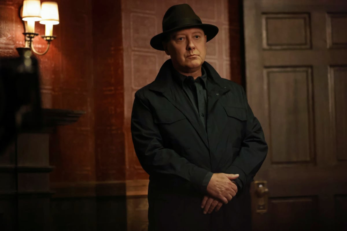 The Blacklist Season 9 comes to Netflix in October. Raymond Reddington wears a black hat and coat and stands with his arms crossed in front of him.