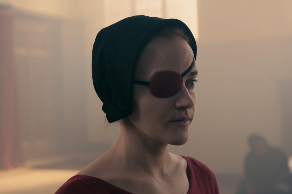Madeline Brewer as Janine in The Handmaid's Tale Season 5. Janine wears a red dress and eyepatch and a black bonnet to cover her hair.