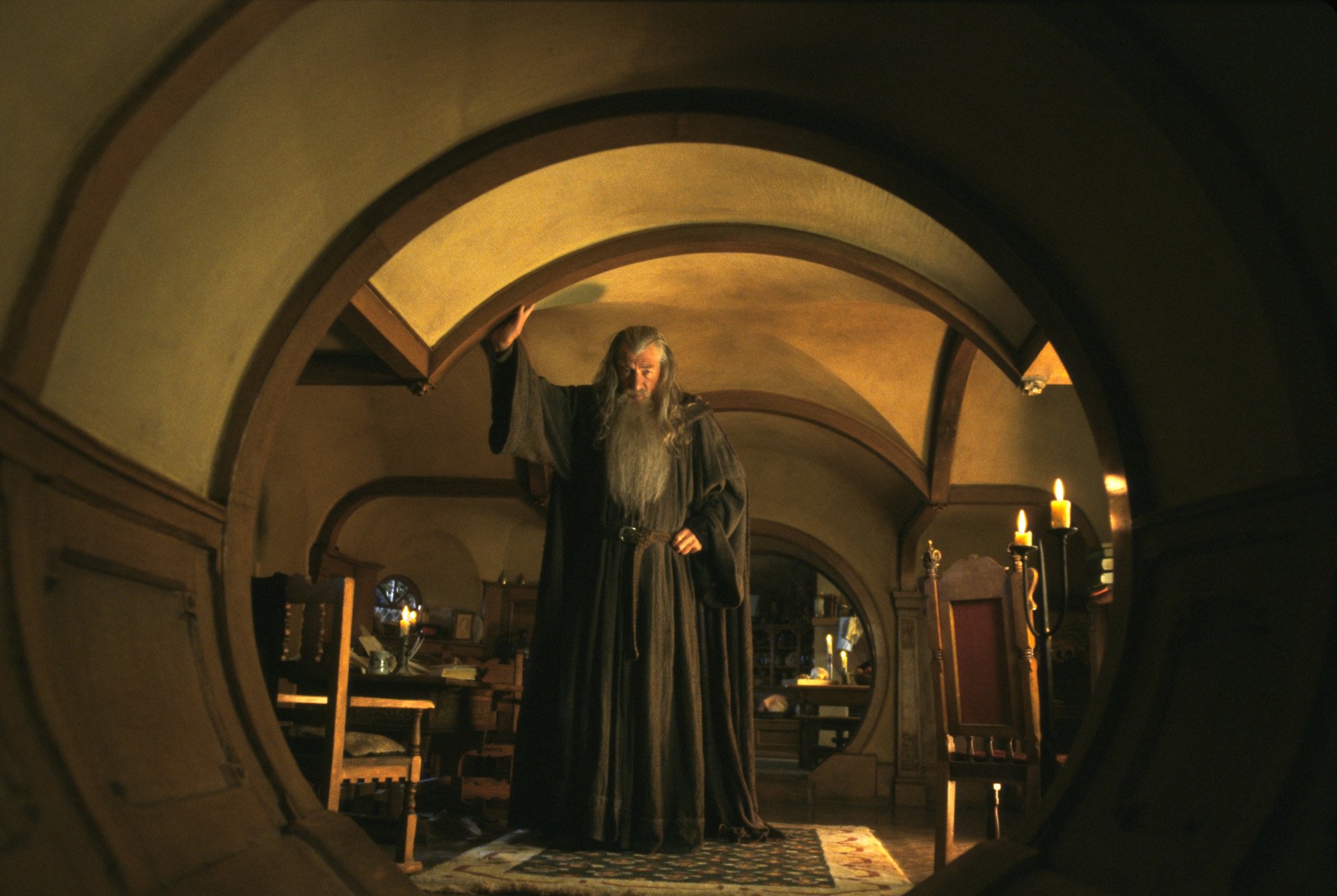Sir Ian McKellen as Gandalf in The Lord of the Rings for our article on when he came to Middle-earth. He stands in a hobbit house and touches the ceiling.