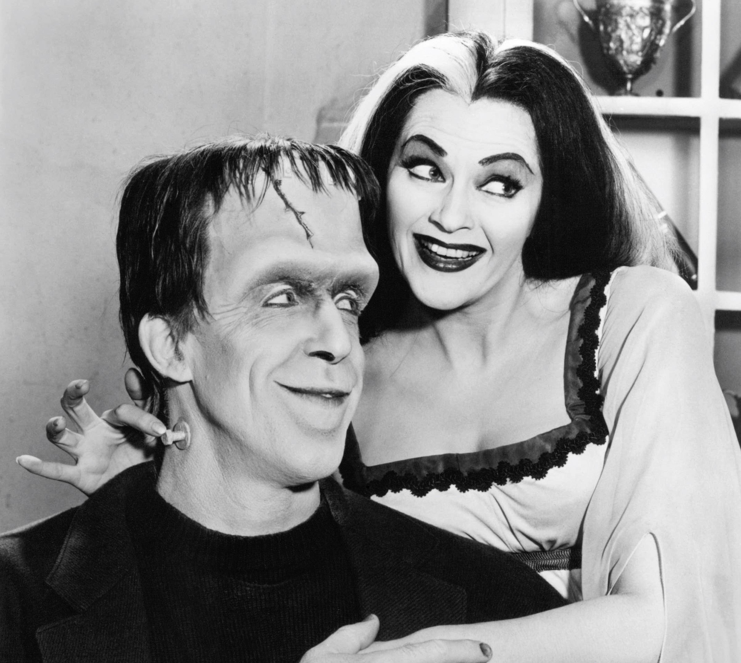 Herman and Lily Munster from 'The Munsters' in front of a cabinet
