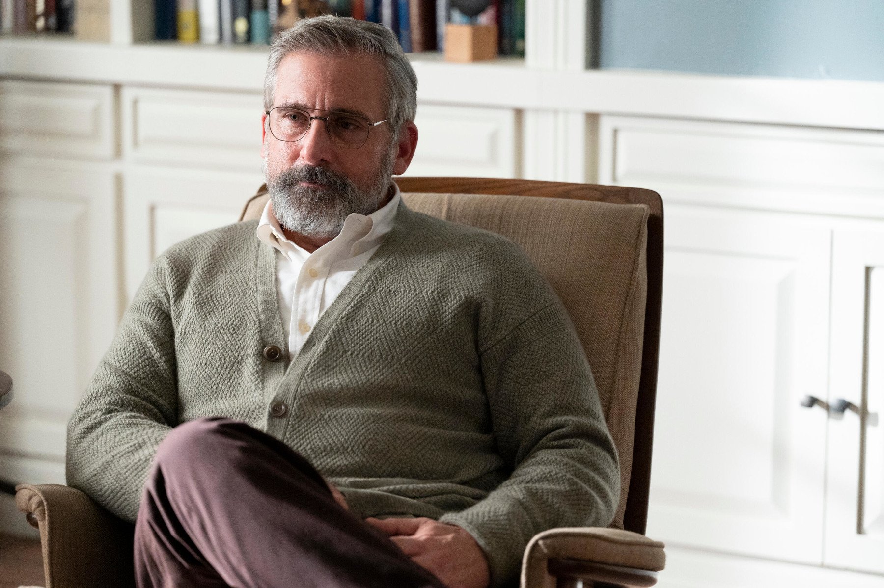 Steve Carell as Alan Strauss in 'The Patient' for our article about episode 7. He's sitting in a chair, wearing a cardigan sweater, and crossing his legs.